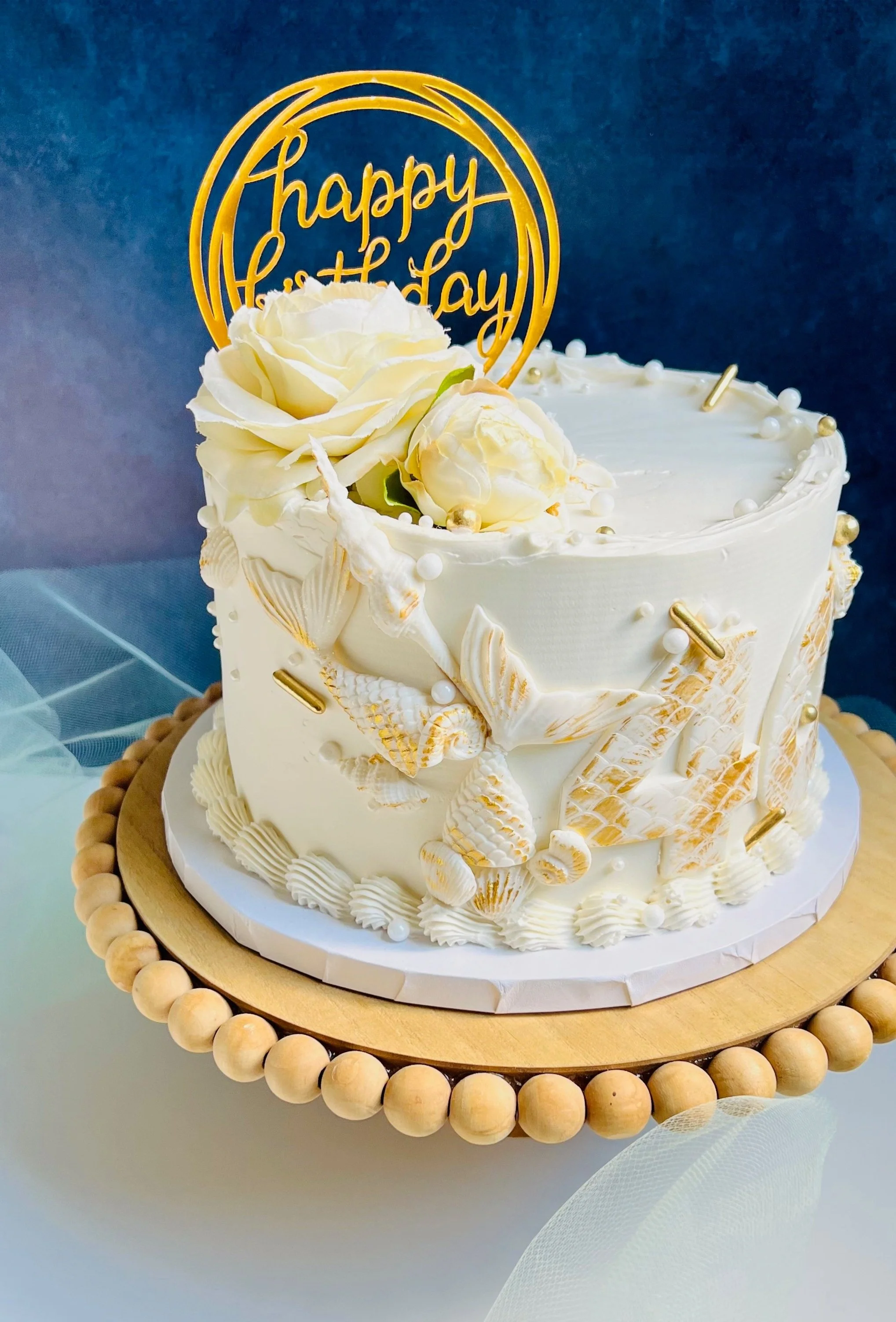 White birthday cake with floral decorations and koi fish designs, topped with a "Happy Birthday" sign, on a wooden cake stand in Plymouth MA.