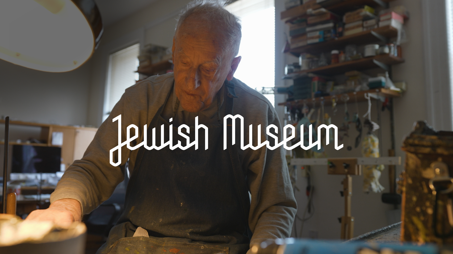Elderly man crafting in a workshop, with "Jewish Museum" text overlay.
