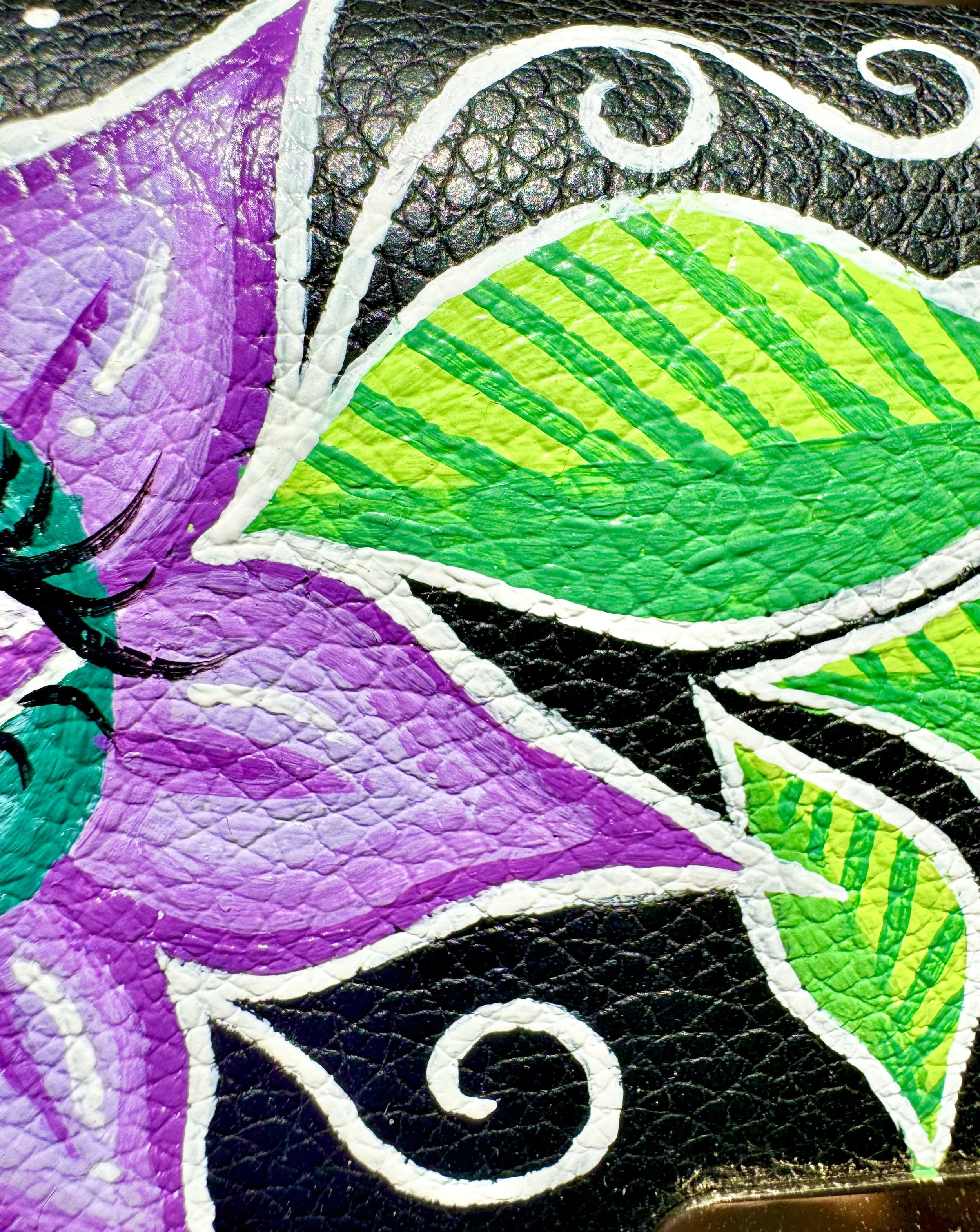 Close-up of colorful street art painted on textured leather surface, featuring purple petals, green leaves with yellow lines, black and white accents.