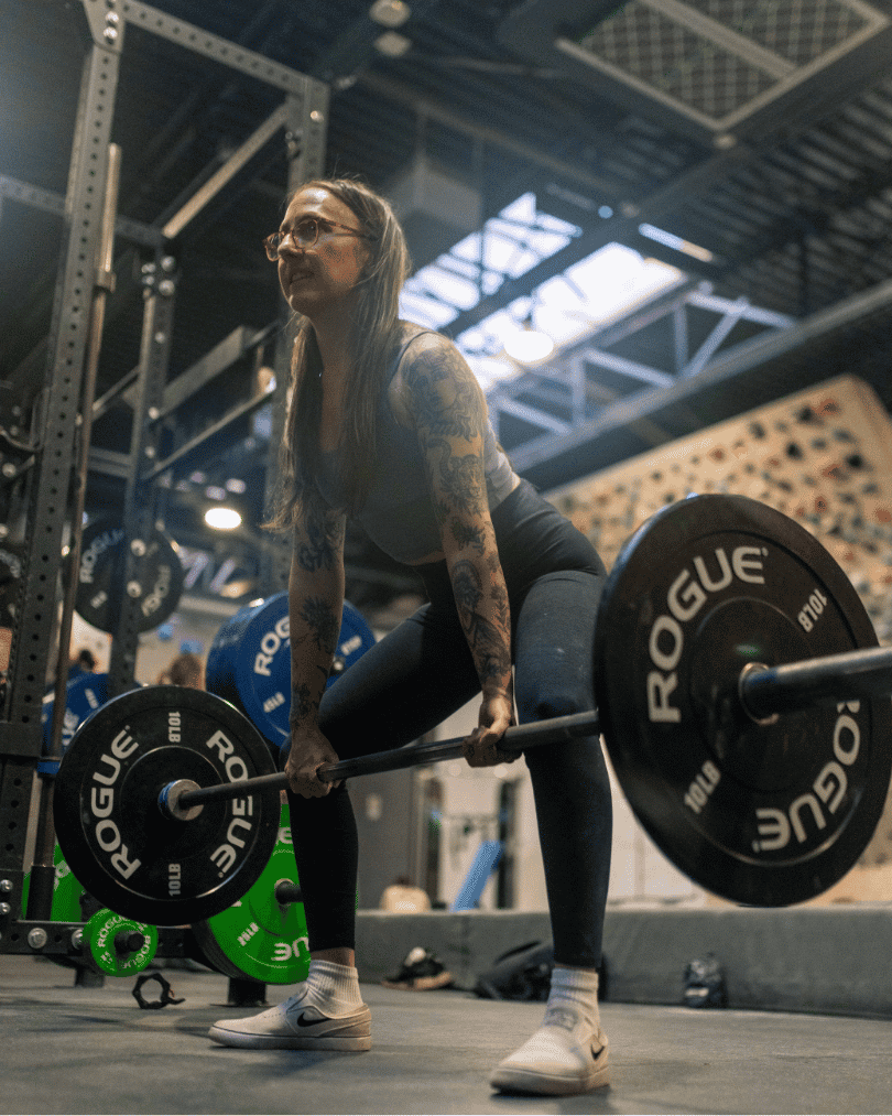 Female with long hair halfway through a deadlift with climbing walls visible in the background.