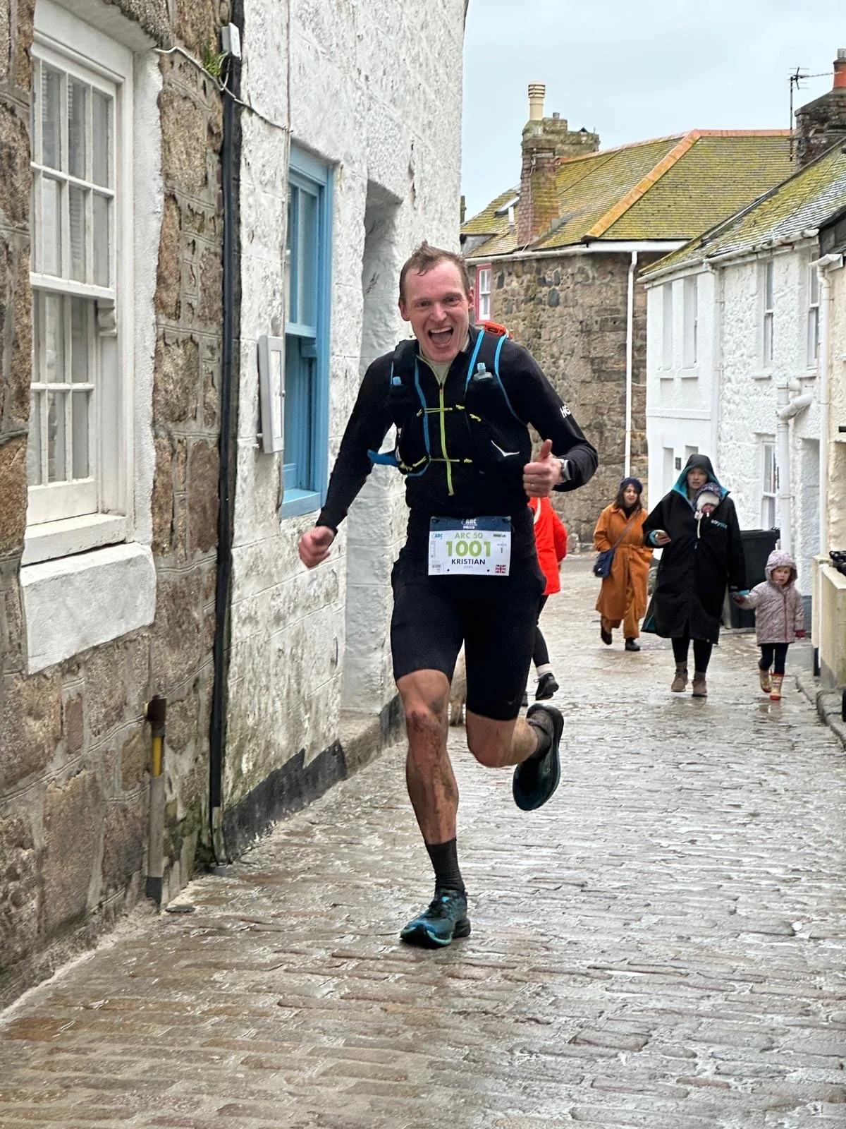 Athlete racing through a Cornish village in the rain, giving a thumbs up