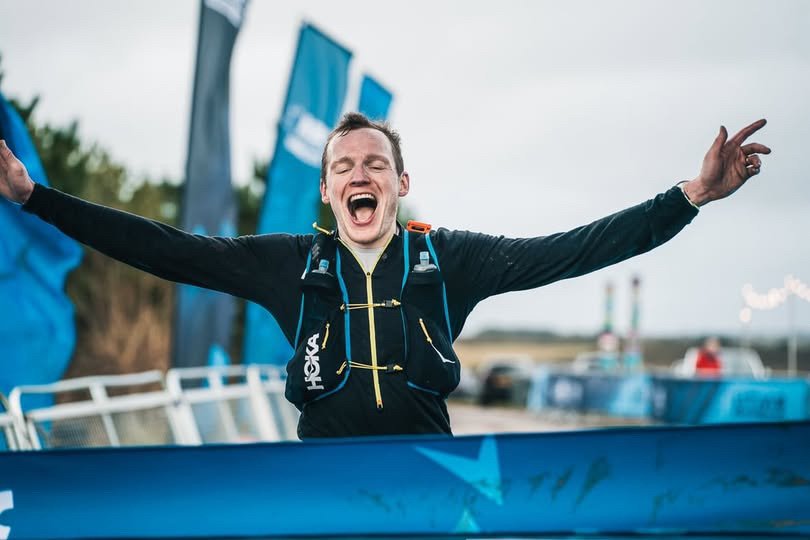 Runner crossing the finish line of a race, with banners behind him