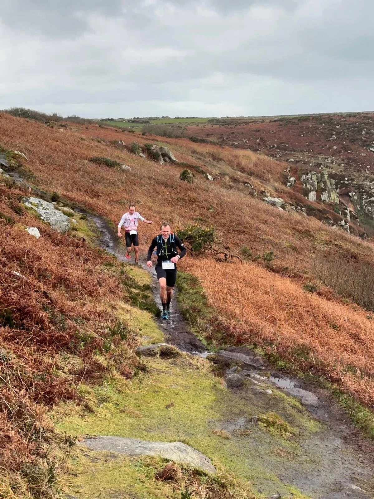 Two trail runners race on the Cornish coast in rainy weather