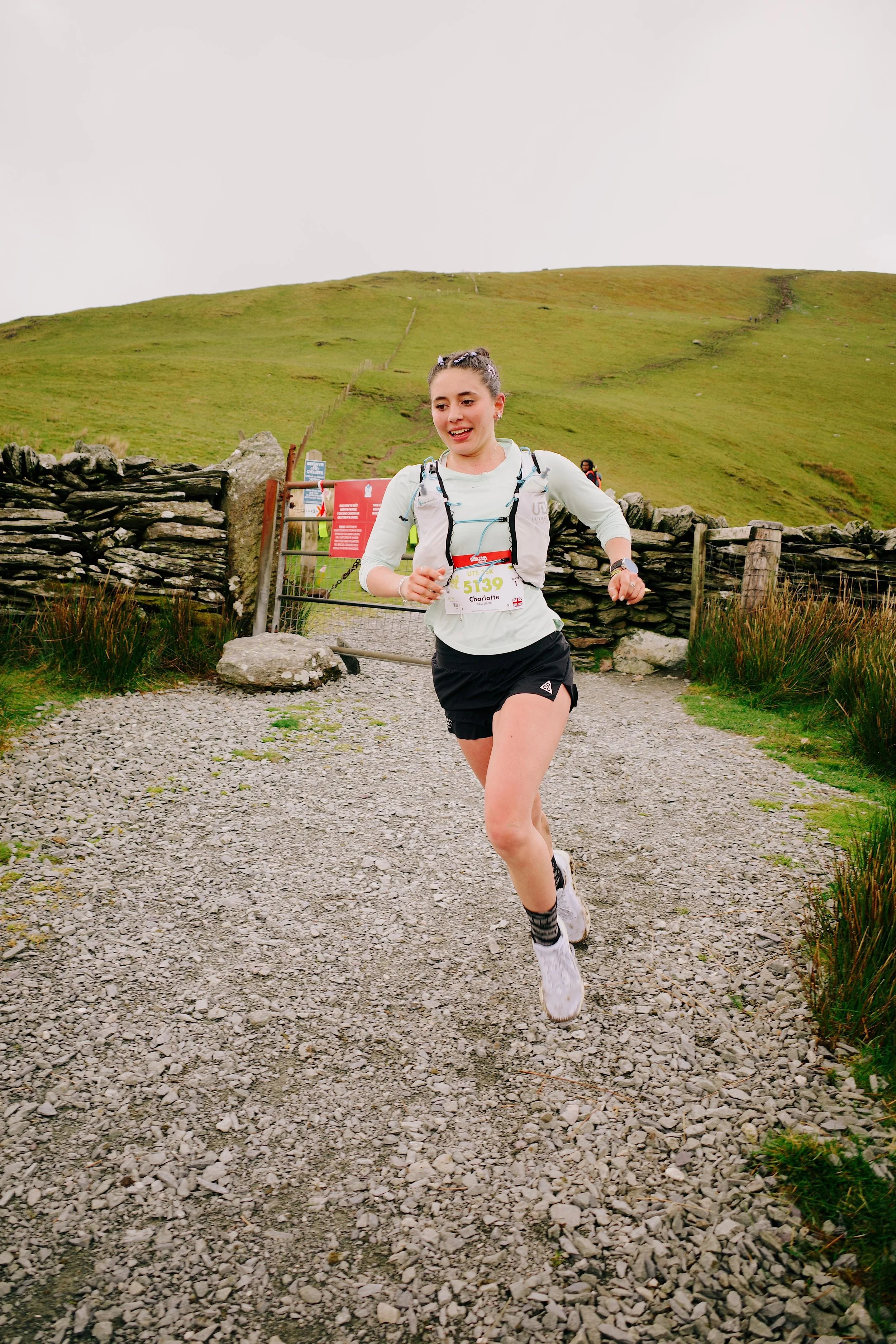 Female trail runner running on a track in front of a gate