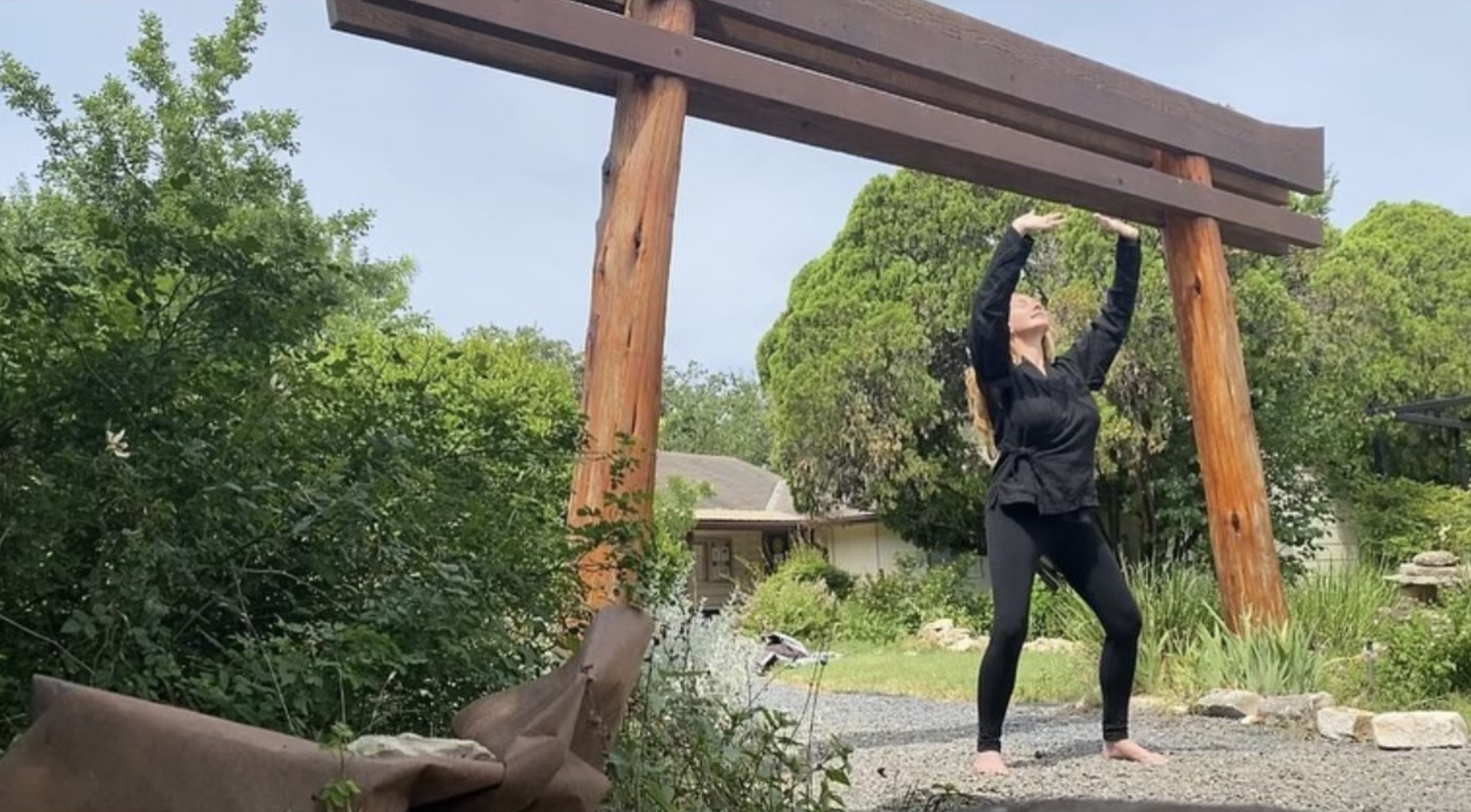 Person practicing martial arts under wooden torii gate in a garden