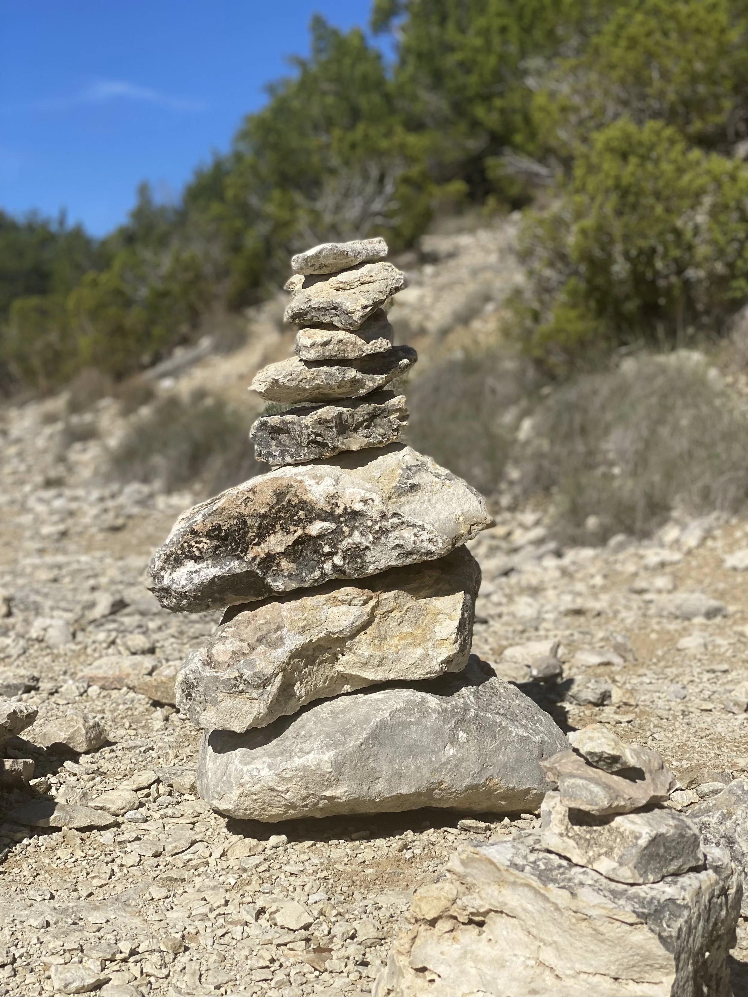 Stack of stones forming a cairn on a rocky path with greenery in the background.