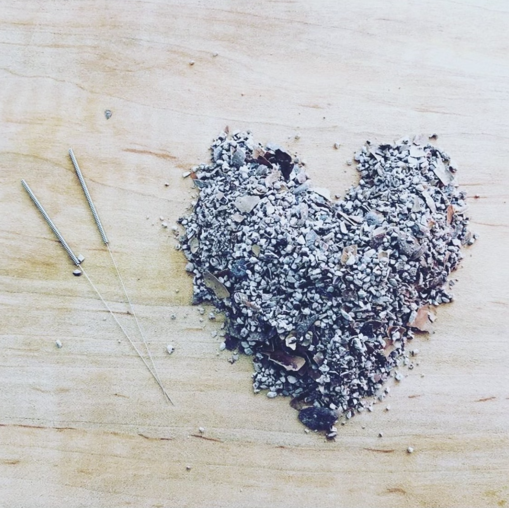 pile of ash in heart shape on wood surface with two acupuncture needles