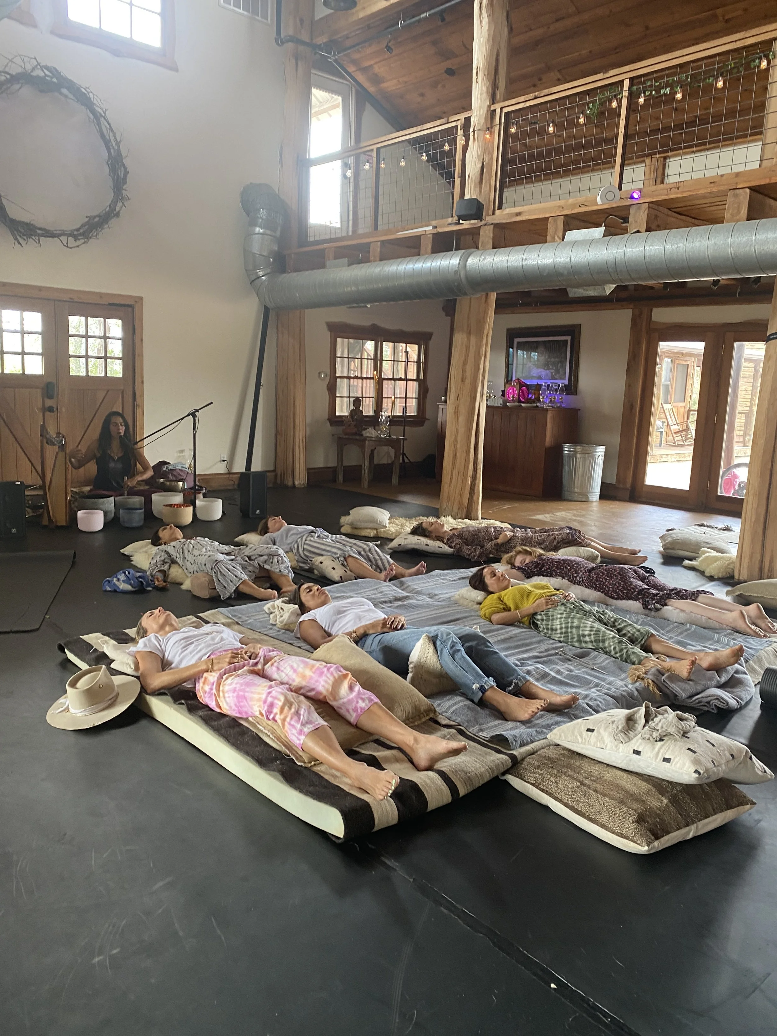 Group of people lying on mats in a wooden interior, possibly participating in a relaxation or meditation session.