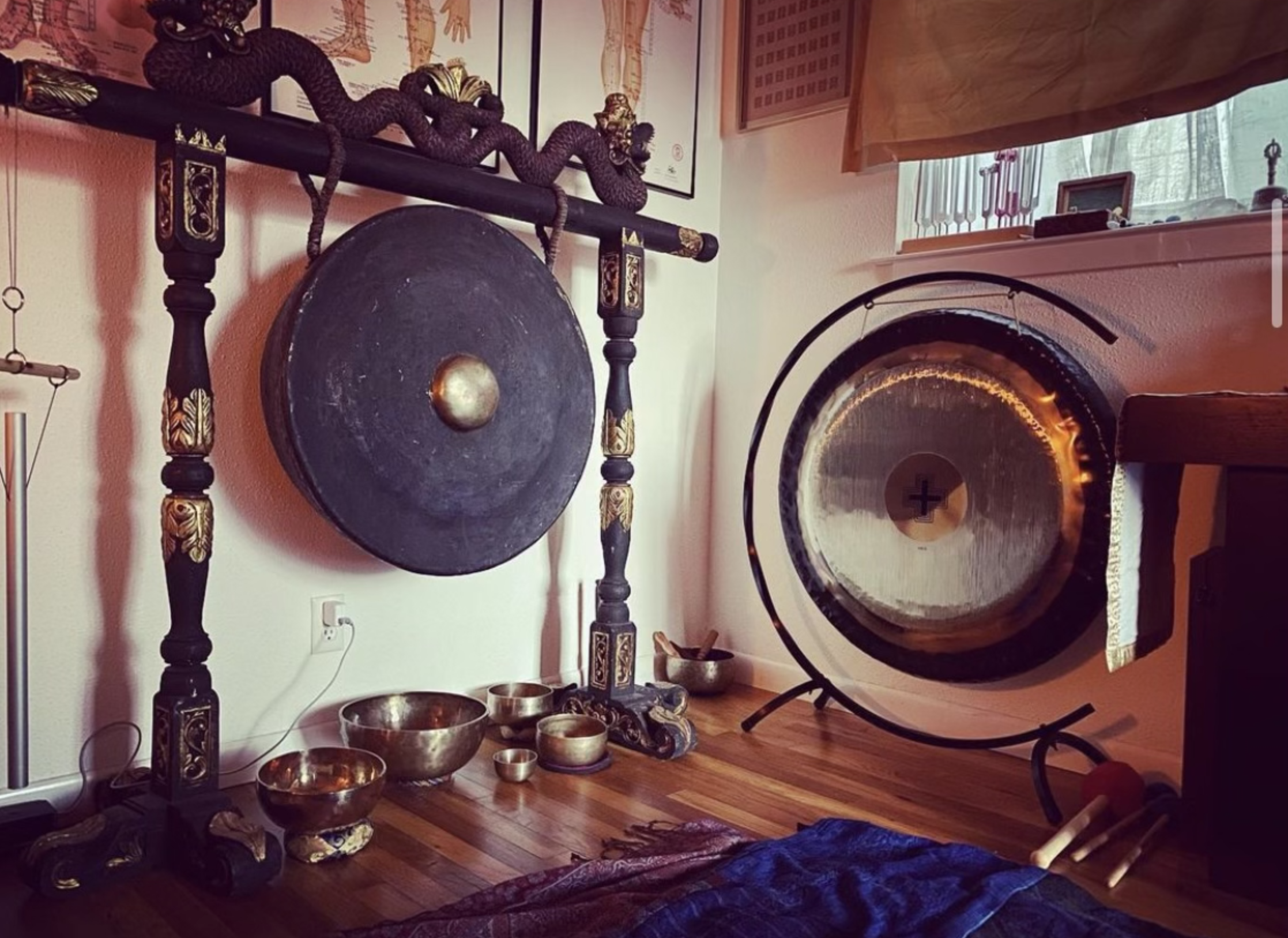 Room with large gongs, Tibetan singing bowls, and percussion mallets on a wooden floor.