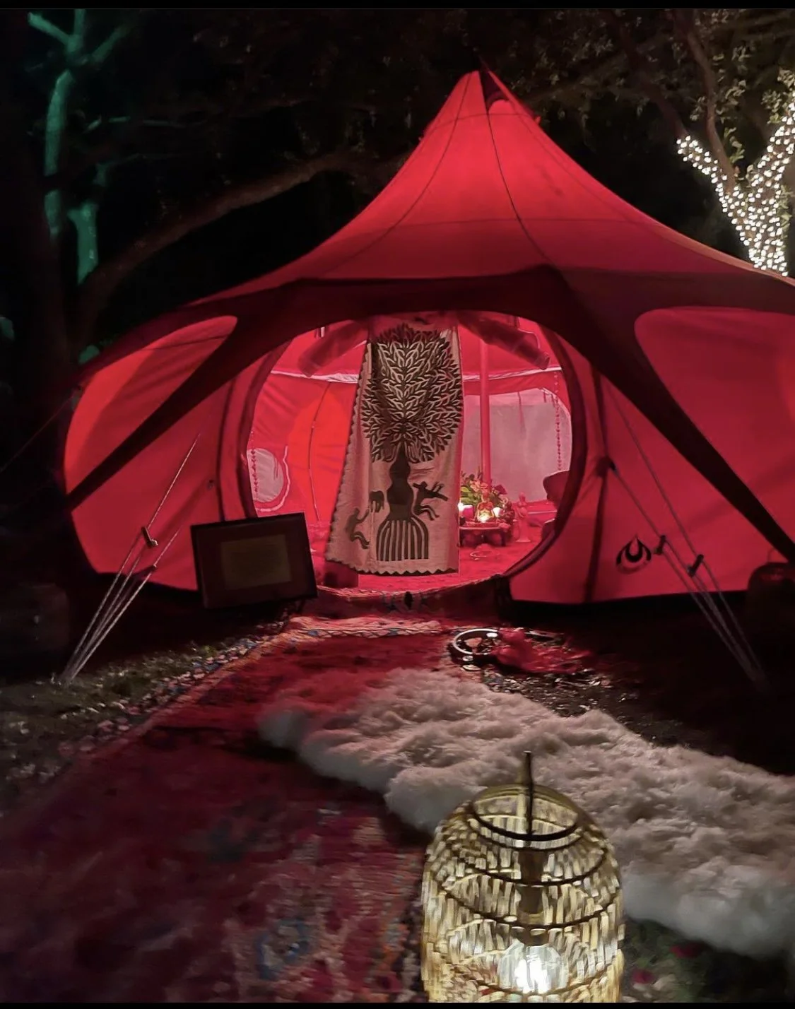 Red tent with decorative artwork, carpet, and lights at night.