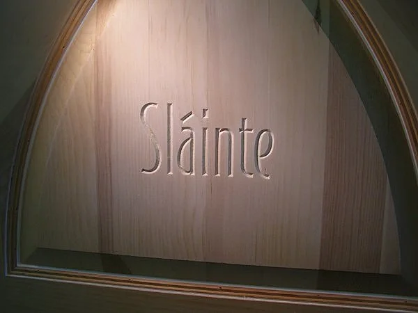 Close-up of a wooden wall with the word 'Slainte' engraved, seen through an arched window or opening.
