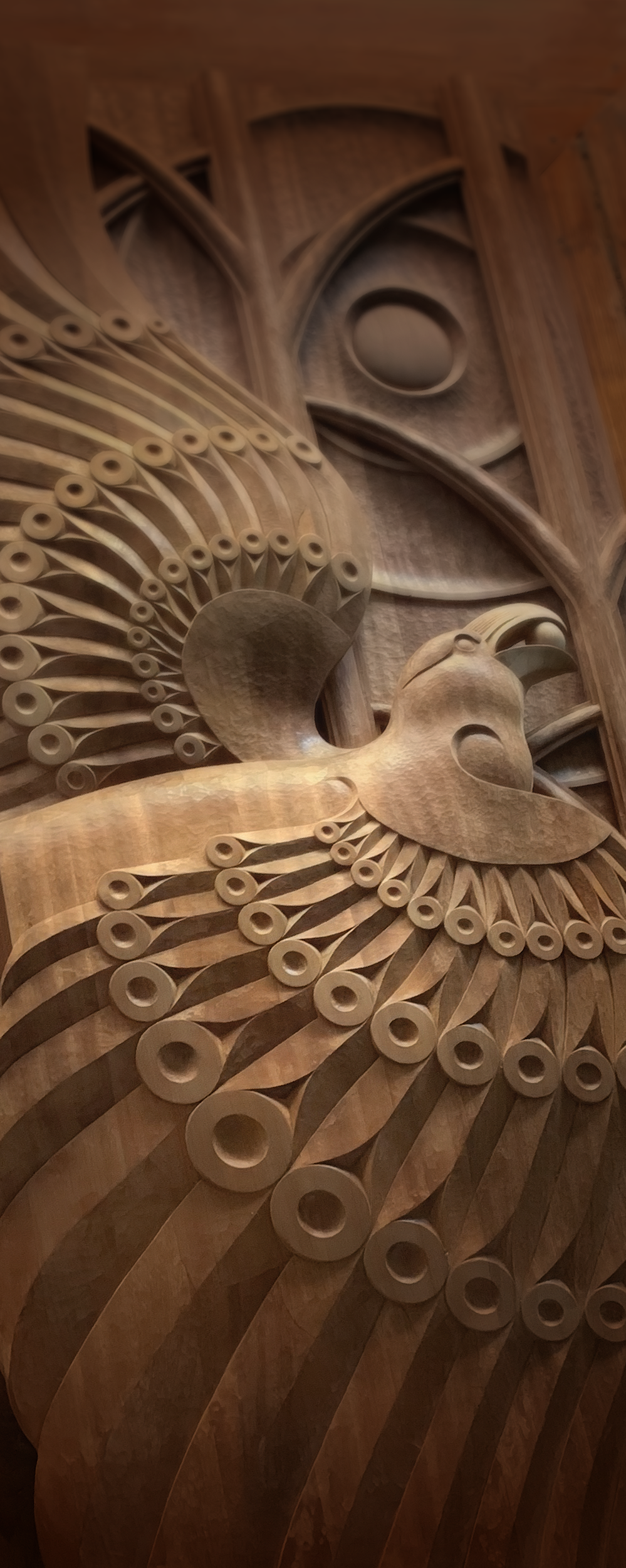 Close-up of a hand-carved raven with radiating feather patterns and a circular sun motif.