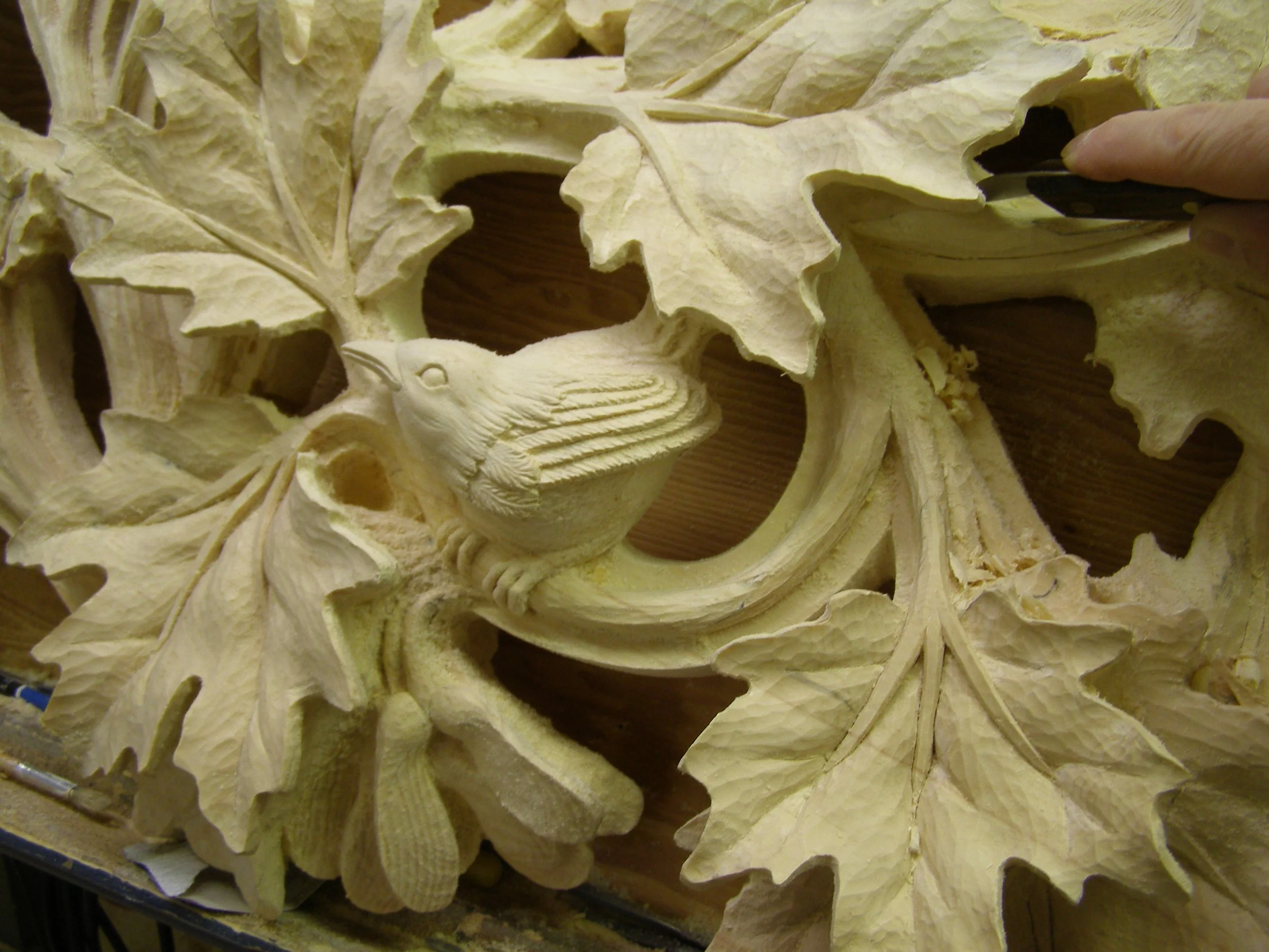 Close-up of a carved wooden sculpture of a bird among autumn leaves.