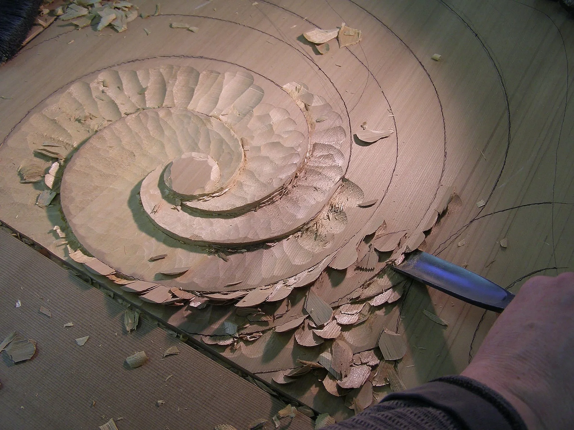 Wood carving process showing hand tools shaping a spiral cedar relief.