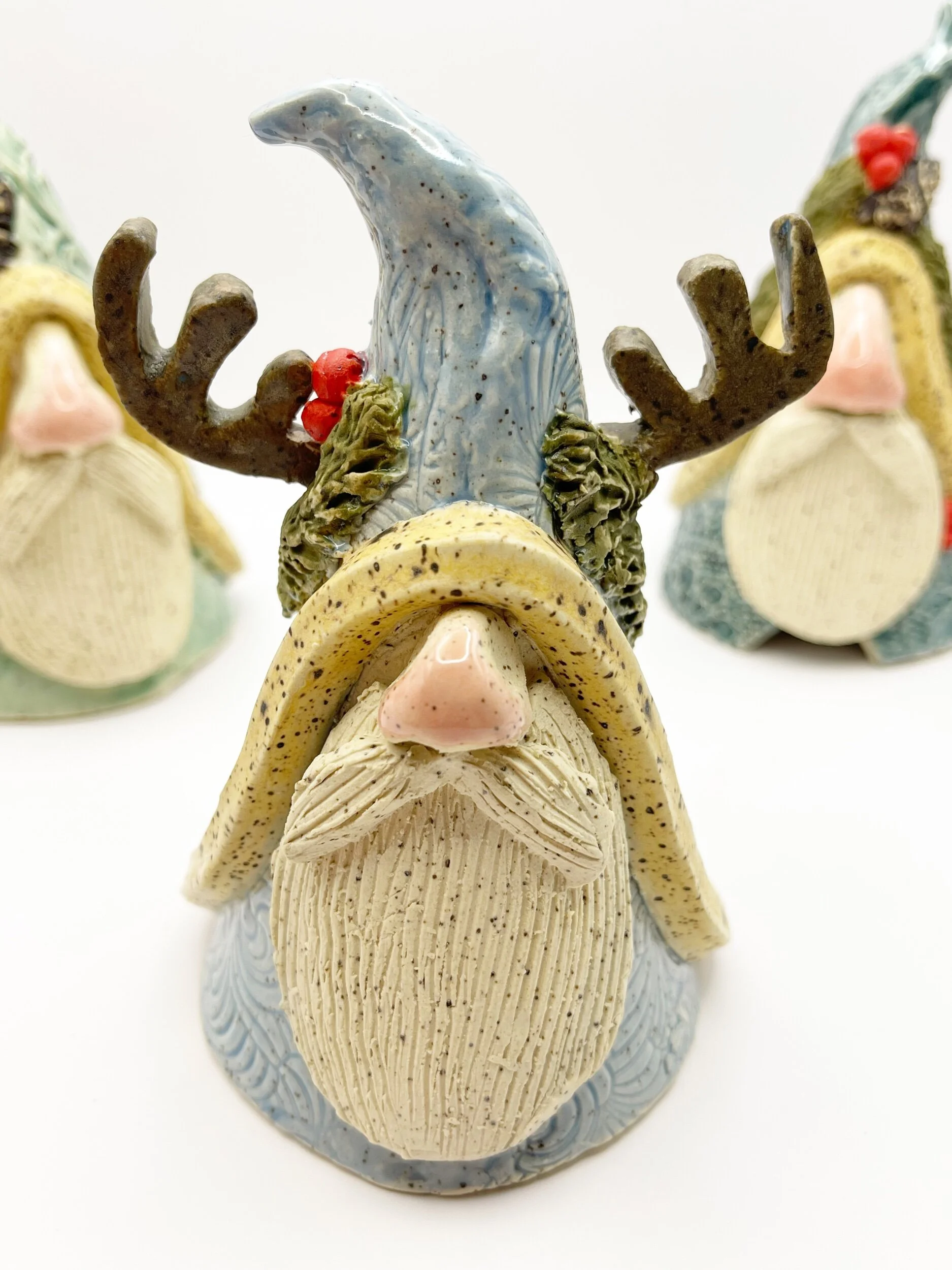 Ceramic Christmas gnome figurine with reindeer antlers, a blue hat, and holly leaves, surrounded by similar figures.