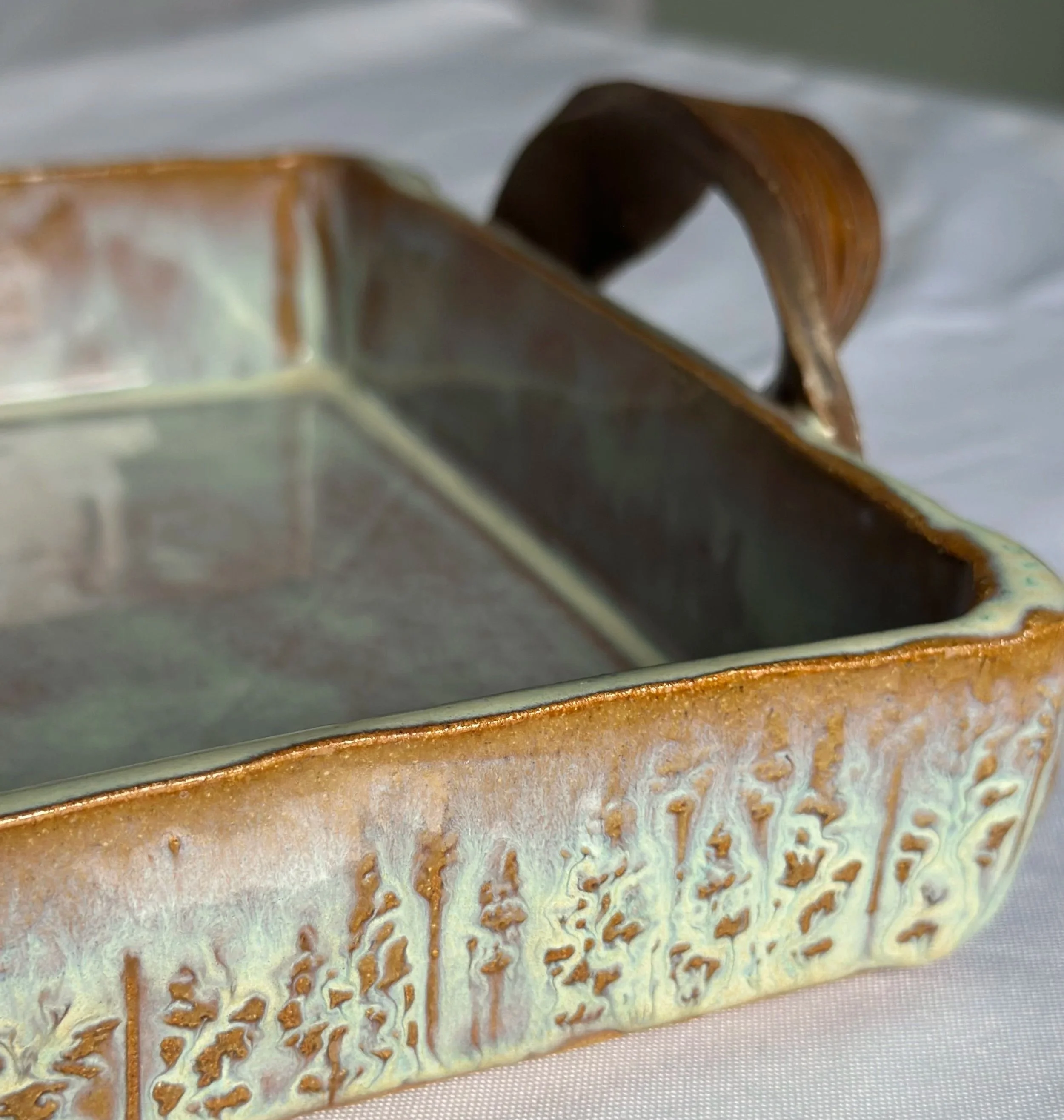 Close-up of a ceramic baking dish with a textured, glazed exterior and a smooth, glazed interior, placed on a light-colored fabric surface.