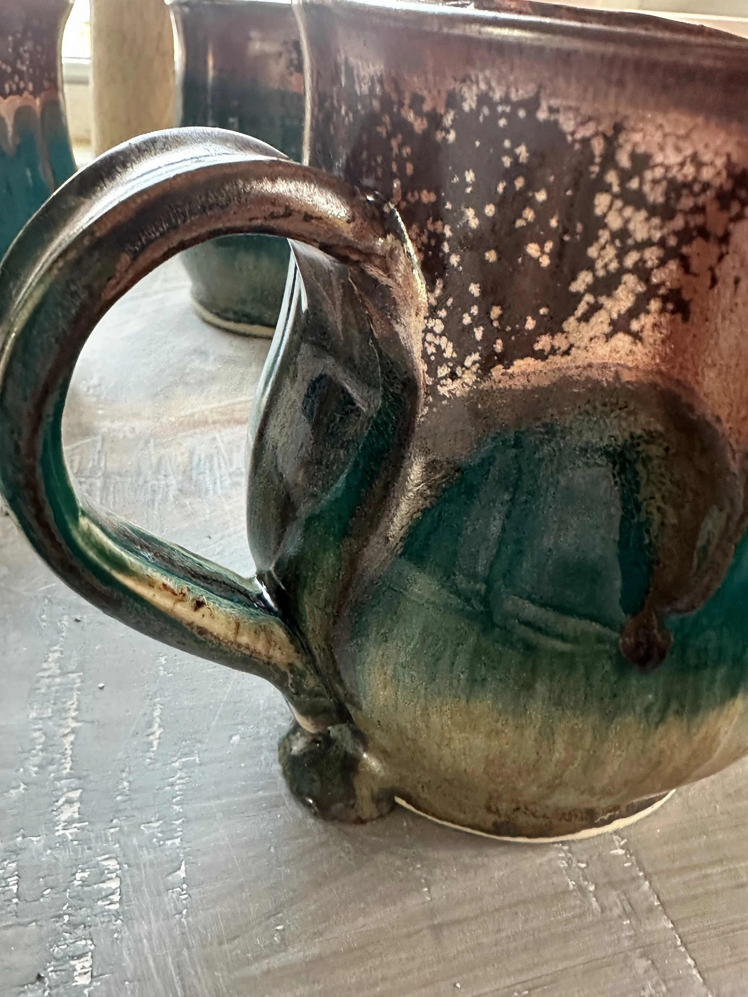 Close-up of a ceramic mug with a green and brown glaze, sitting on a wooden surface.