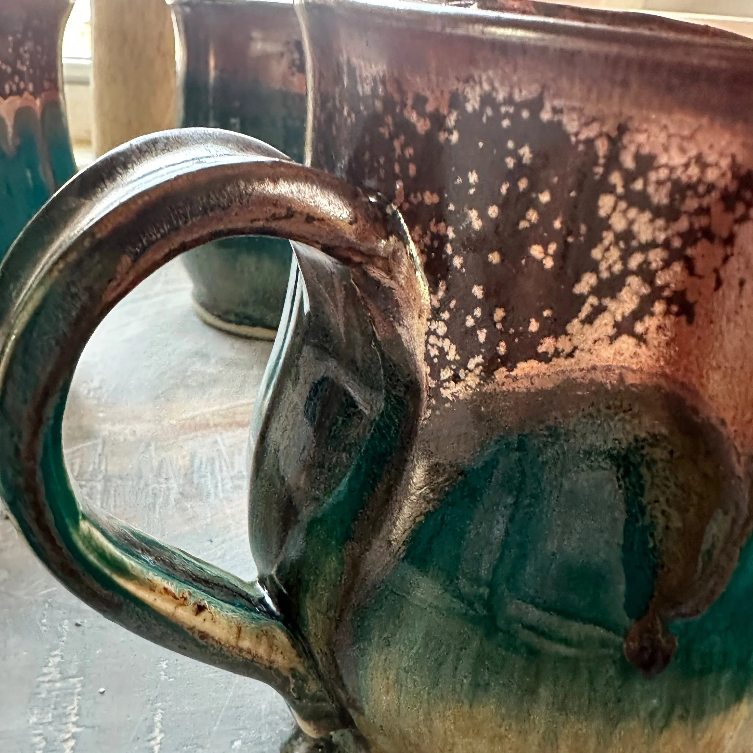 Close-up of a rustic, multi-colored ceramic mug with a dark handle, showing a speckled and textured surface.