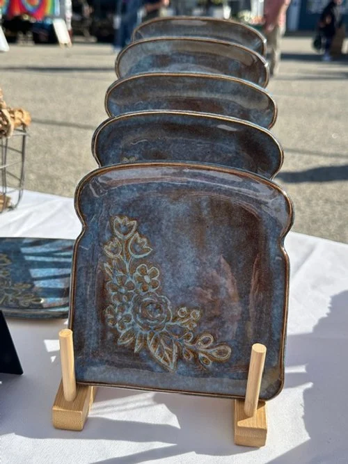 Five ceramic plates with floral designs displayed on a wooden stand at an outdoor market.