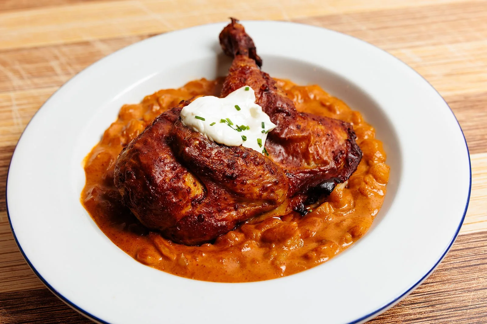 Plate of baked chicken with brown gravy on a bed of beans, topped with a dollop of sour cream and chopped chives.