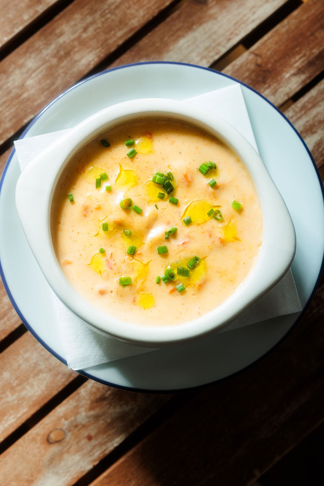Bowl of creamy soup garnished with chopped green onions and drizzled with oil on a white dish, placed on a wooden table.