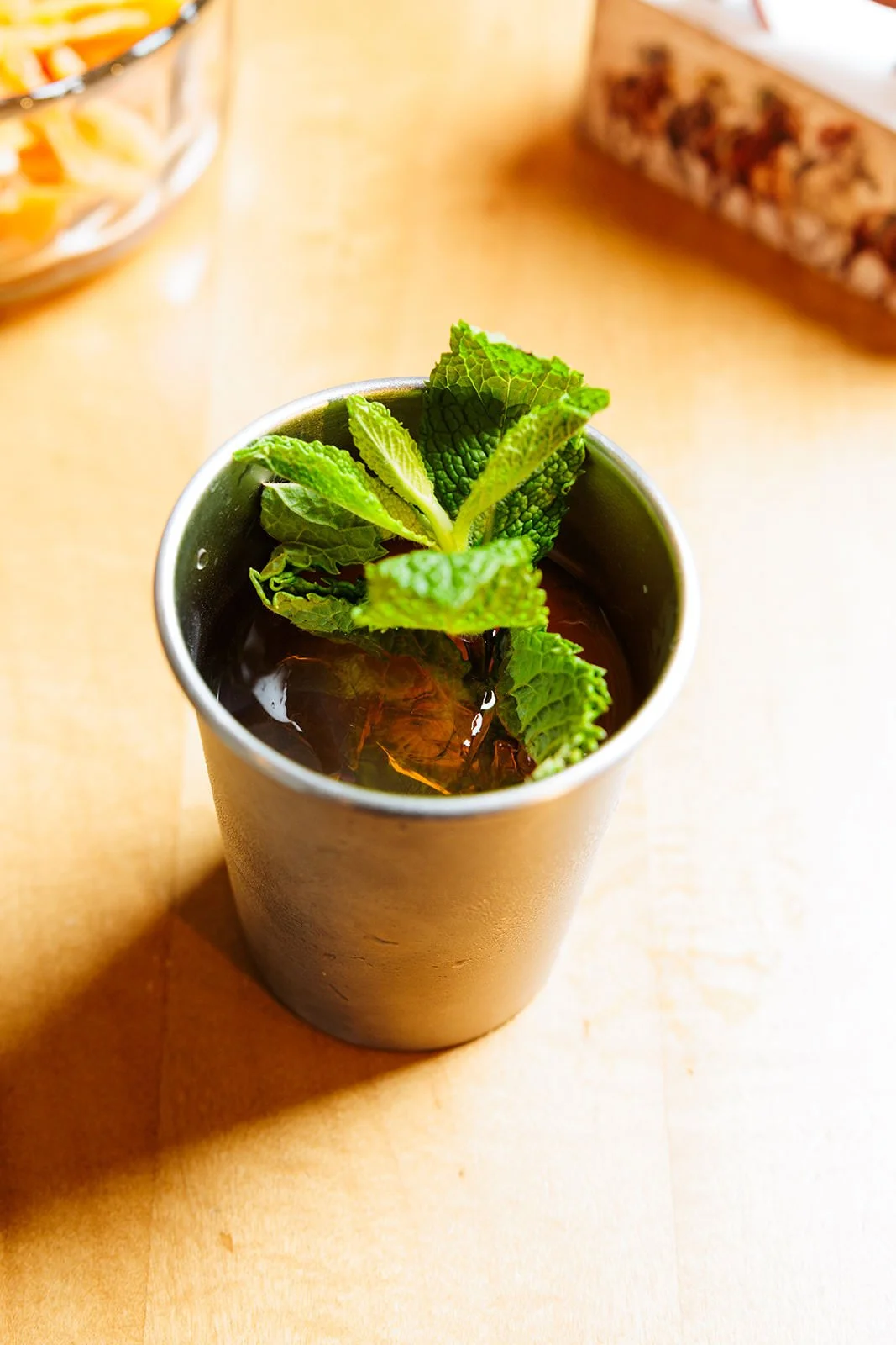 A metal tumbler filled with a dark beverage, garnished with fresh mint leaves.
