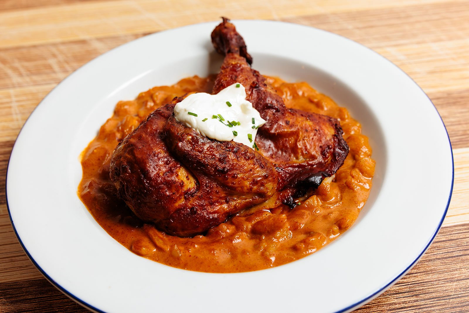 Plate of baked chicken leg quarter with gravy and a dollop of sour cream garnished with chopped chives, served on a bed of beans
