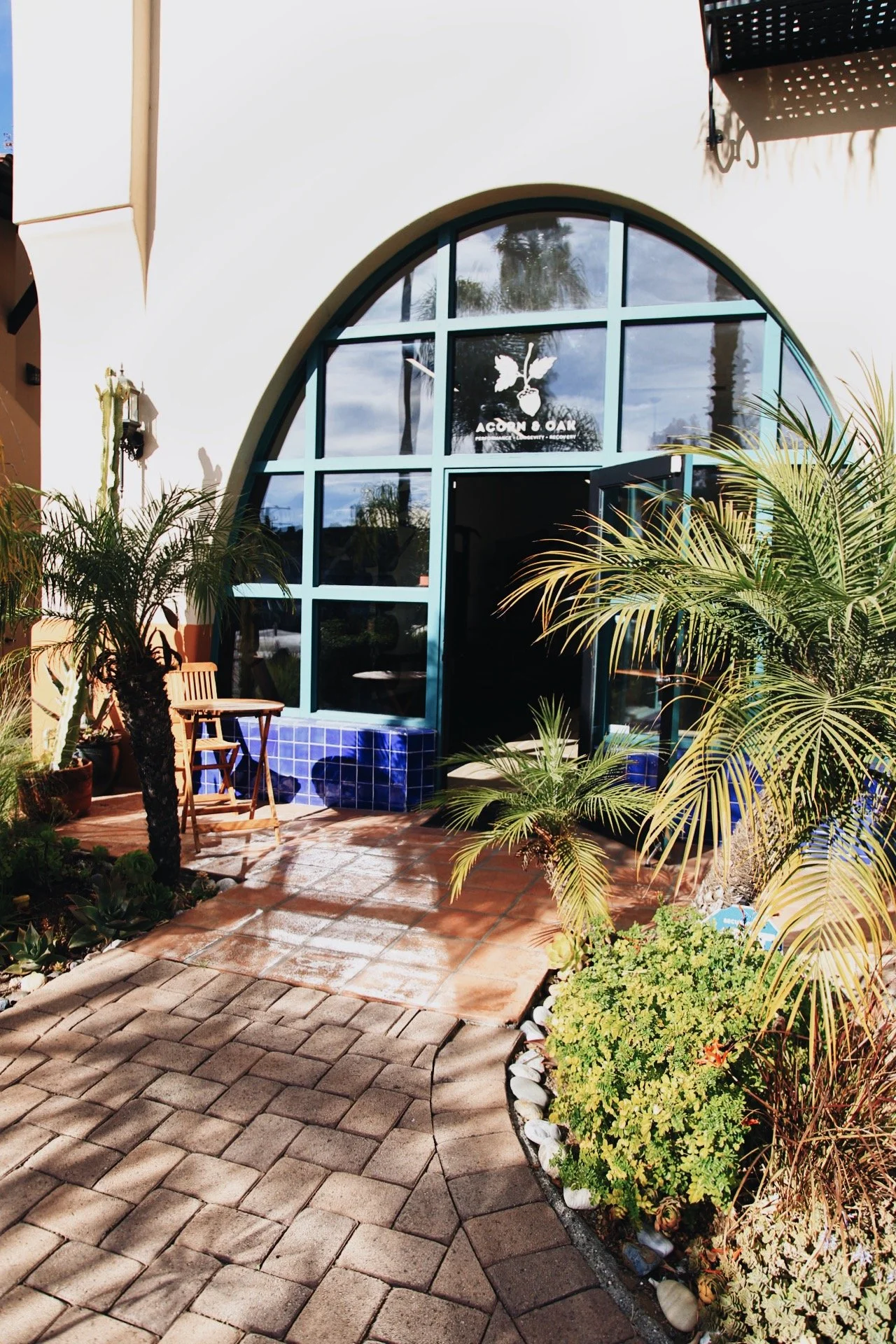 Acorn & Oak’s arched front entrance, with the logo above the open door, blue tiles and palms.