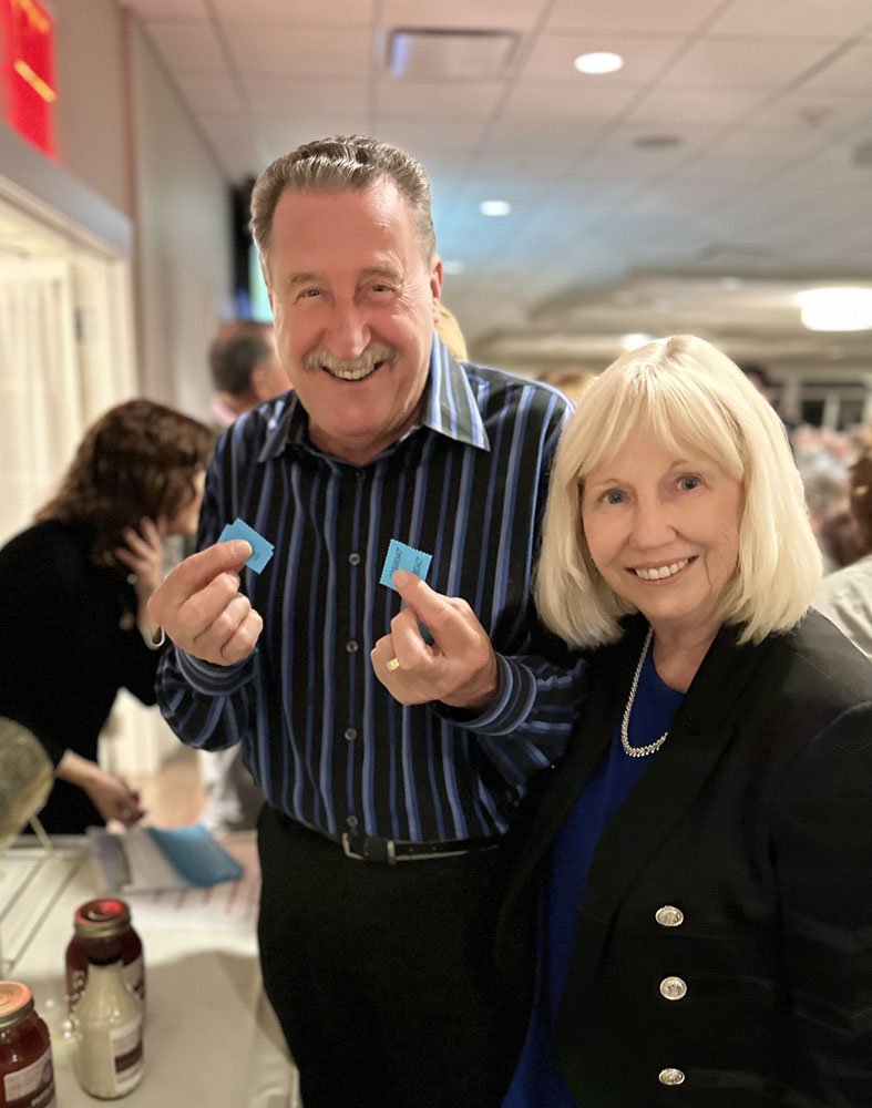 Two people smiling and holding blue tickets at an indoor event.