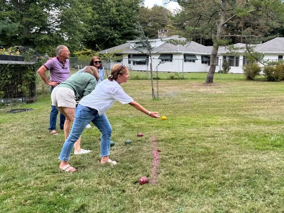 Four metallic lawn bowls on a sandy playing surface with a grassy field in the background.