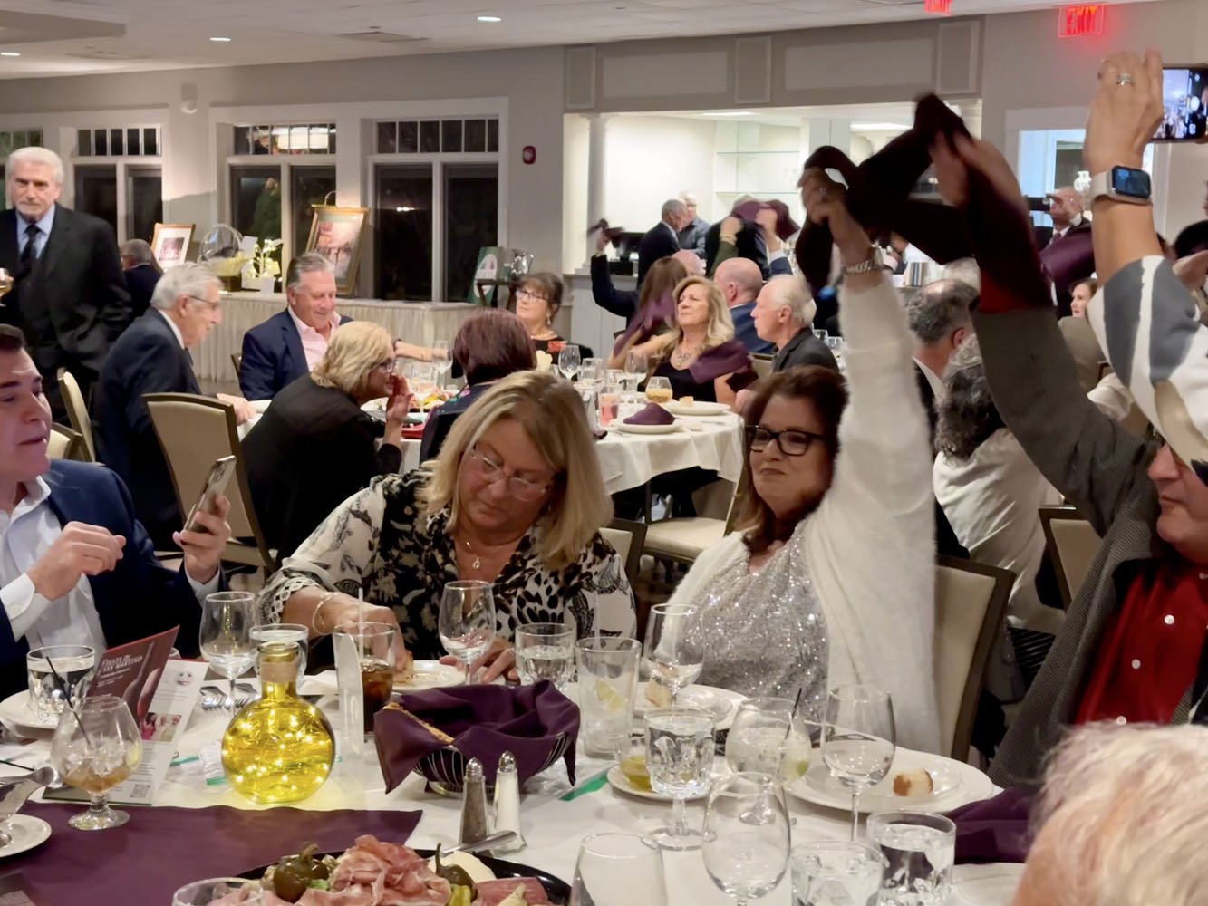 Guests at a formal dinner event with some holding napkins in the air.
