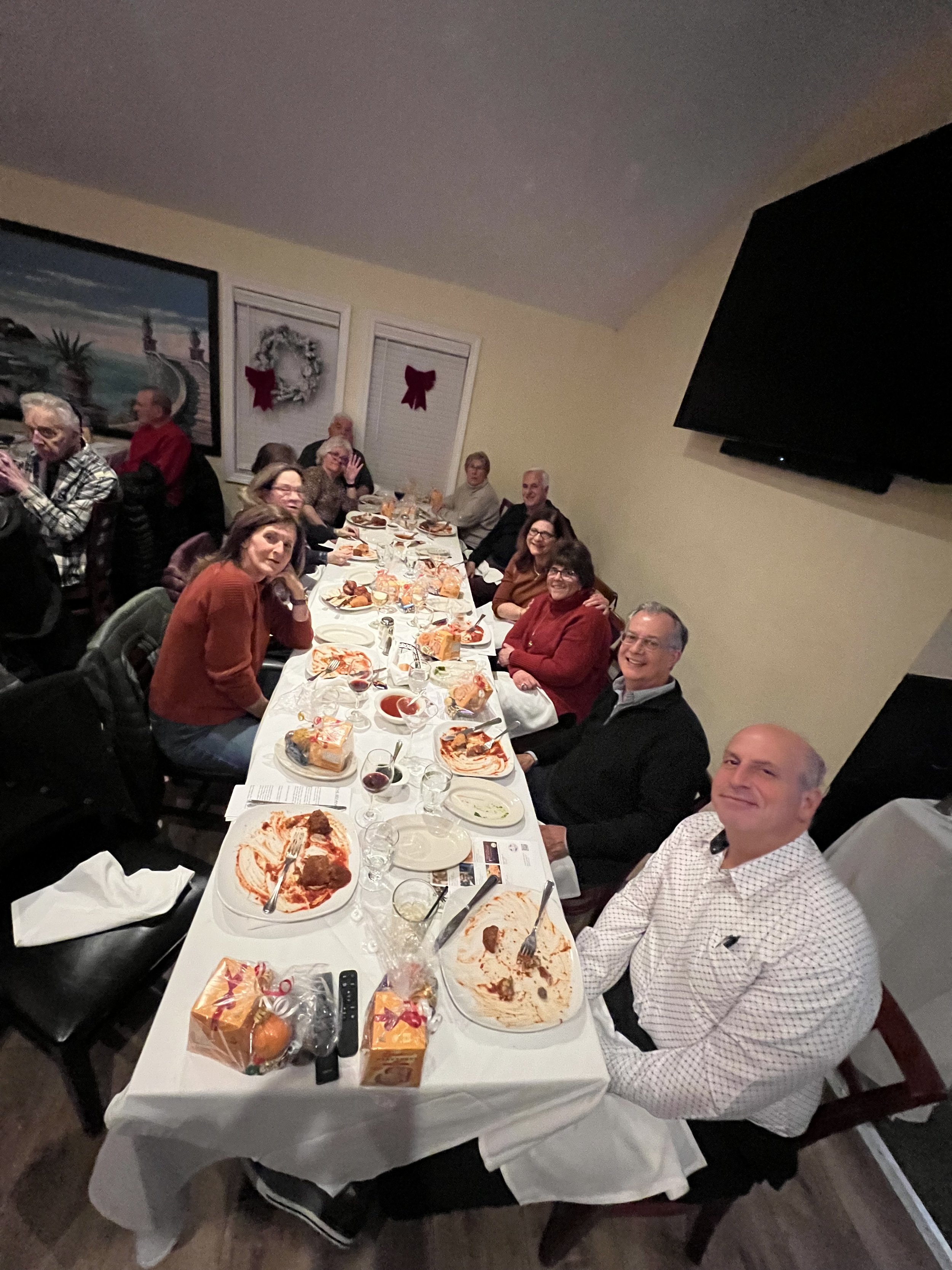 Group of people gathered around a dinner table inside a restaurant, with empty plates and gift boxes on the table, engaging in a social gathering.