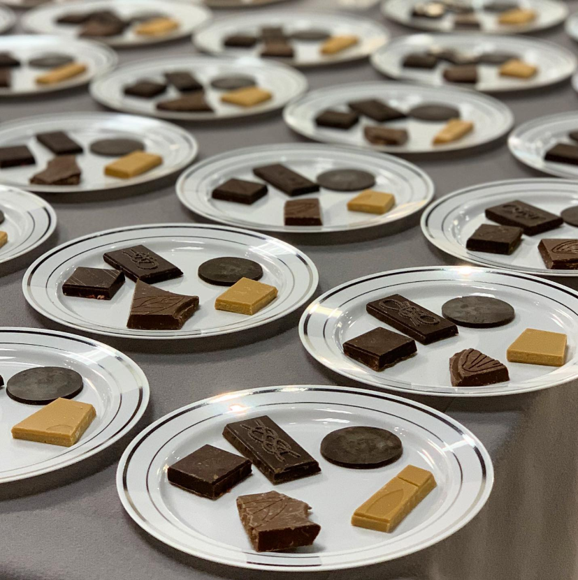 Multiple white plates arranged in a grid, each holding a variety of chocolates and cookies.