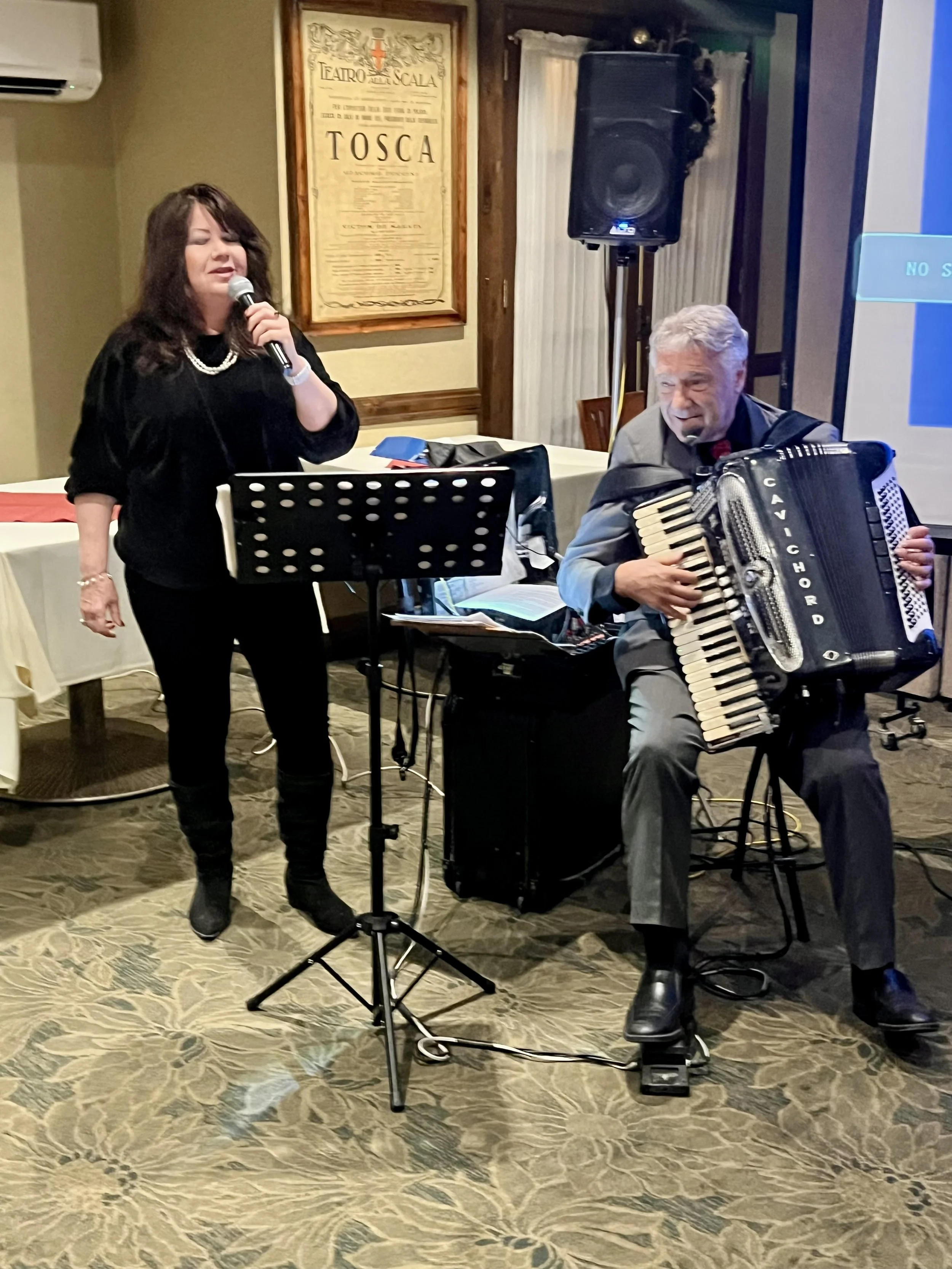 A woman singing into a microphone and a man playing an accordion during a musical performance in a restaurant or event space.