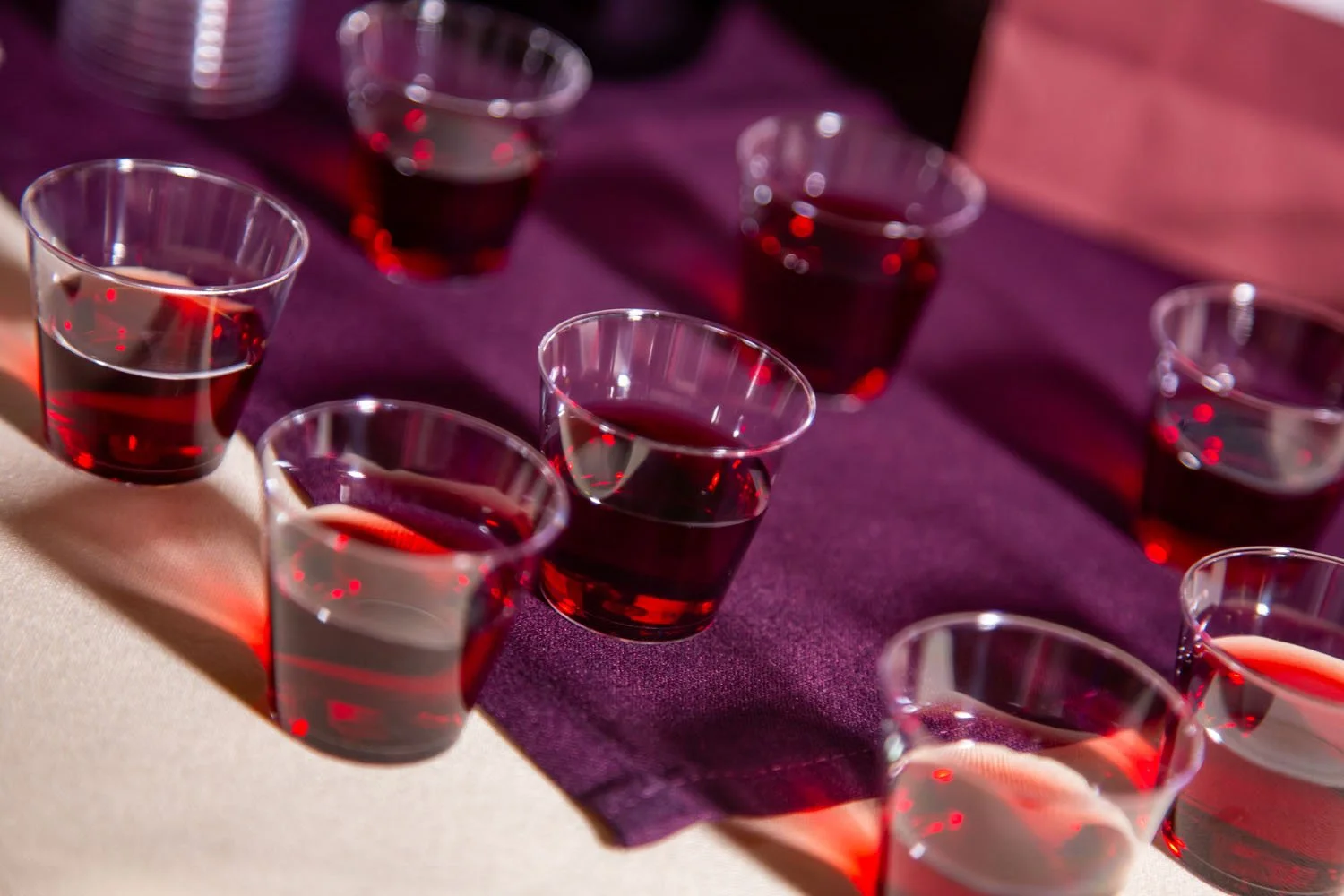 Multiple shot glasses filled with red wine on a purple tablecloth.
