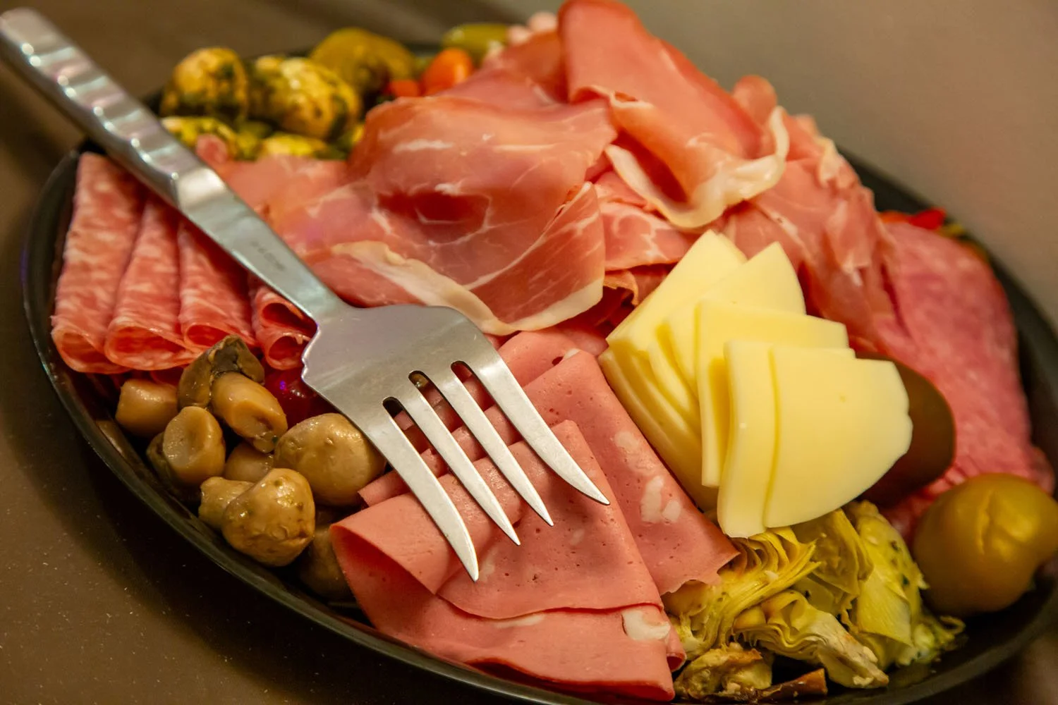 Plate of assorted deli meats including ham, salami, and turkey, topped with slices of cheese, green olives, and roasted vegetables.
