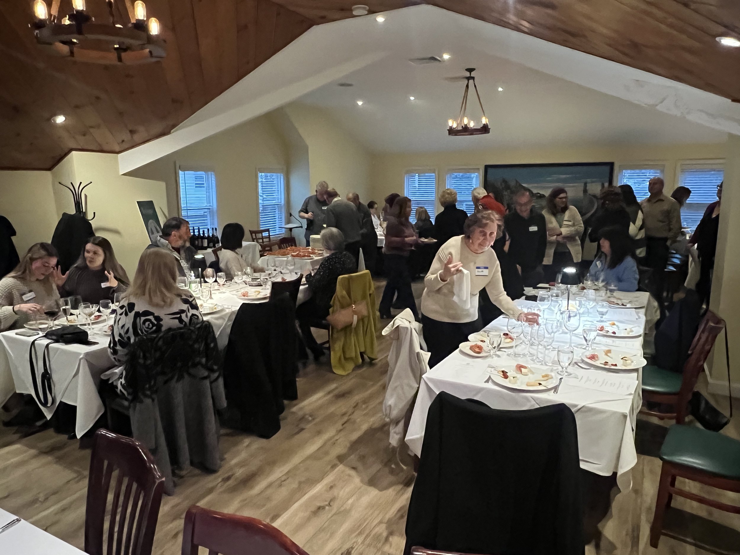 Indoor social event in a restaurant with people sitting and standing around tables, eating and talking.