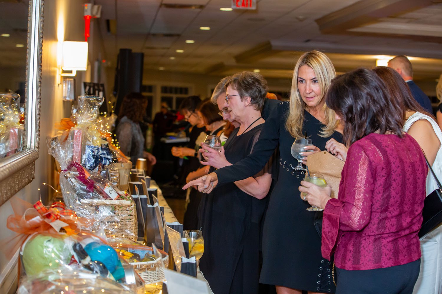 People at a charity auction browsing gift baskets and items on display.