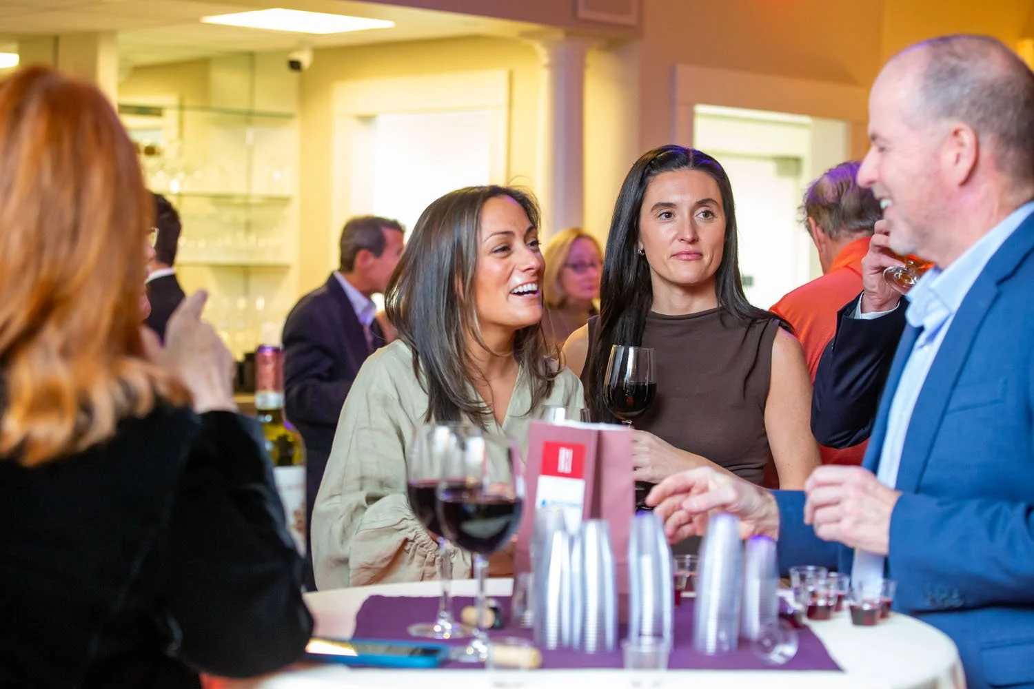 Group of people socializing at a bar or restaurant, drinks on the table, engaged in conversation.
