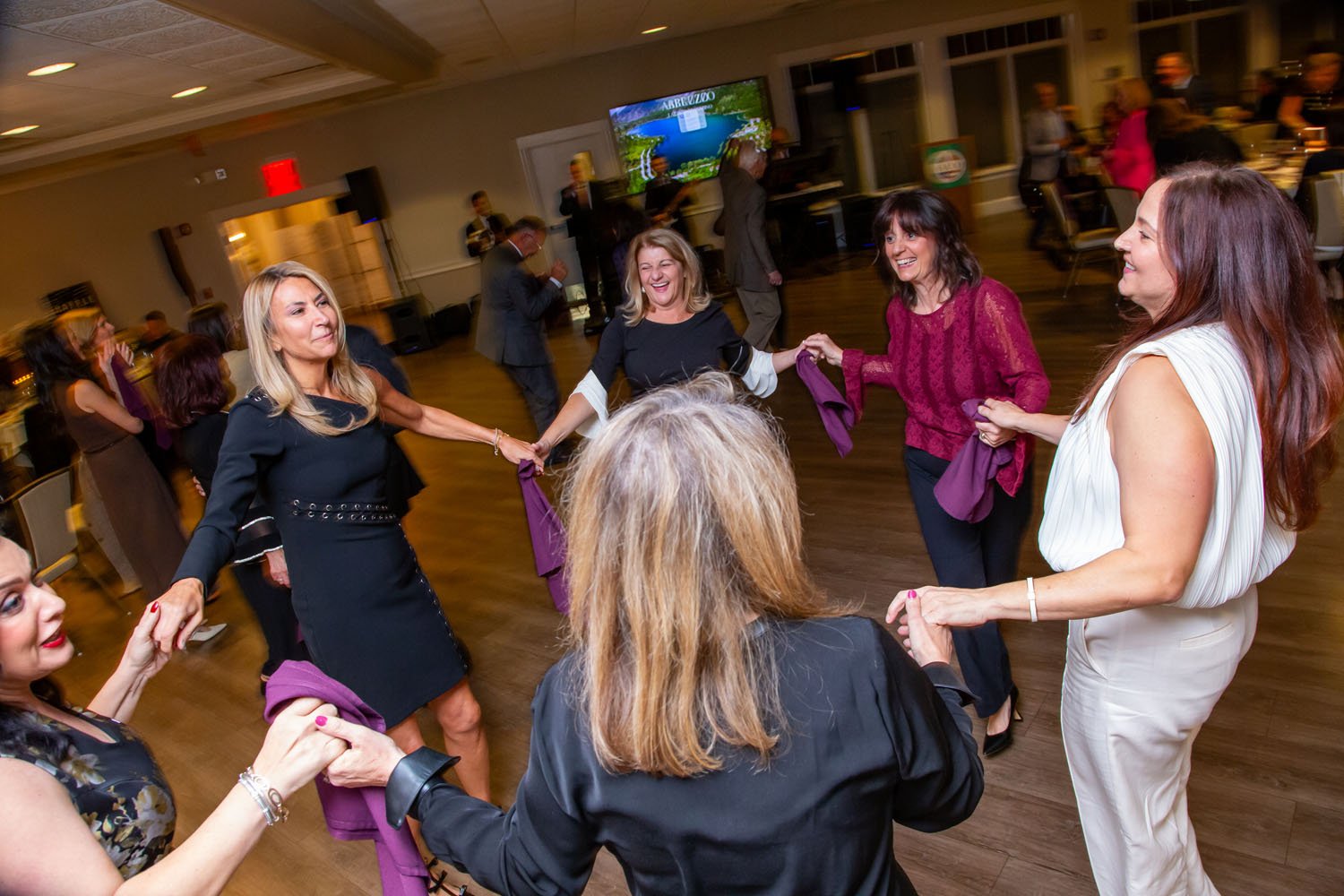 Women holding hands and dancing in a circle at an indoor social event or party.