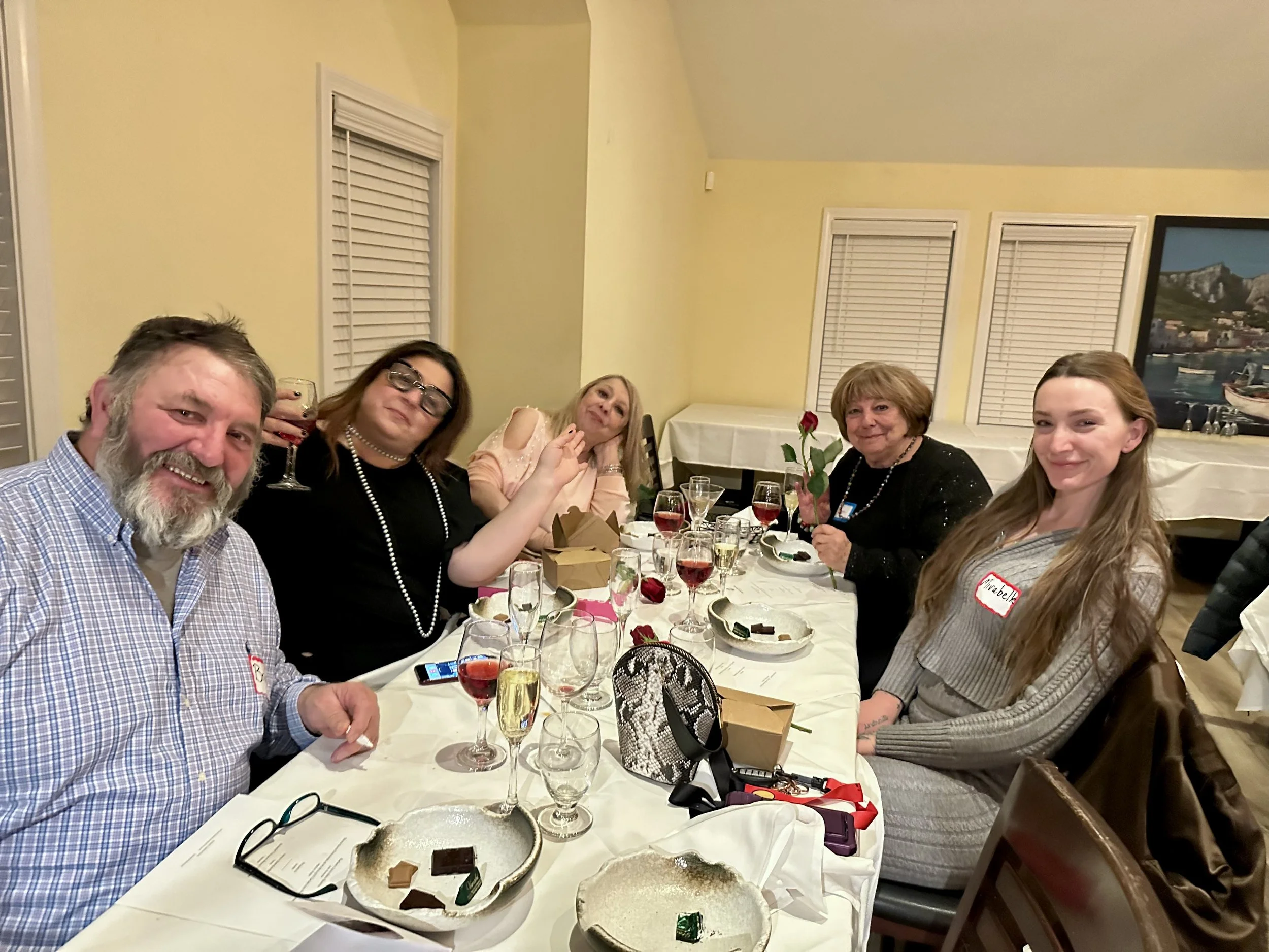 Five people sitting at a banquet table during a celebration, with glasses of wine and desserts, in a decorated dining room.