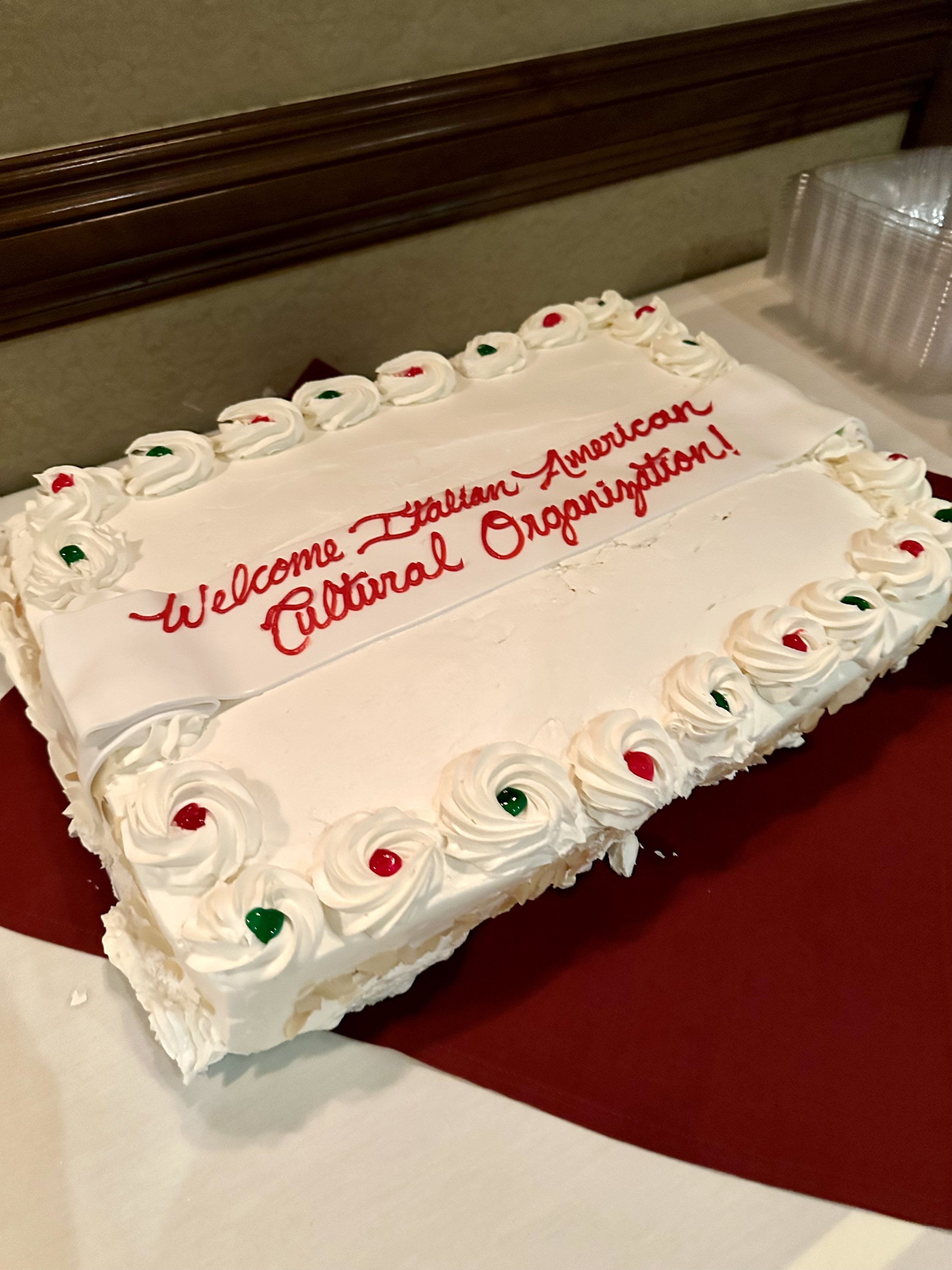 Rectangular cake with white frosting, decorated with red and green dots, and text reading "Welcome Italian American Cultural Organization."