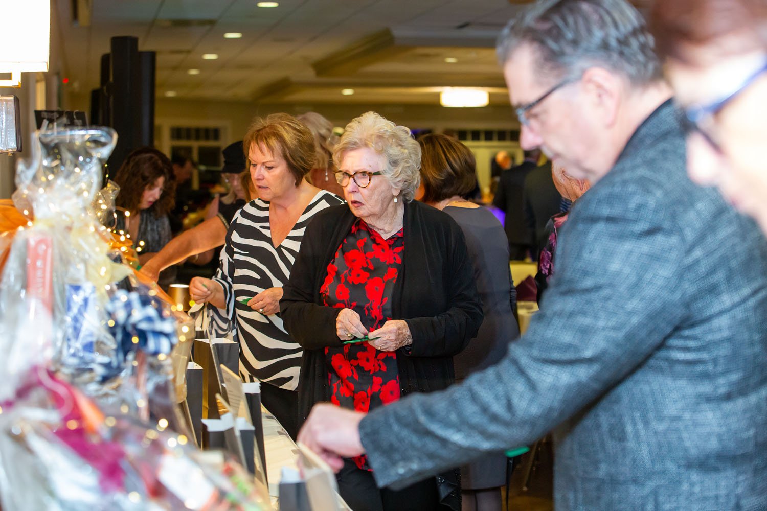 People shopping at a holiday gift table at an indoor event, with women looking at wrapped presents and decorations.