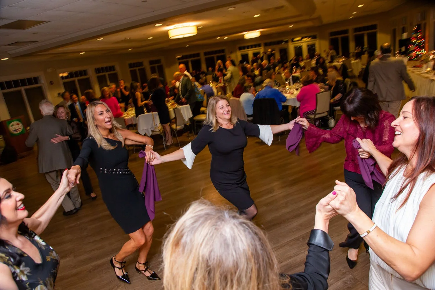 People dancing and celebrating at a holiday party in a banquet hall.