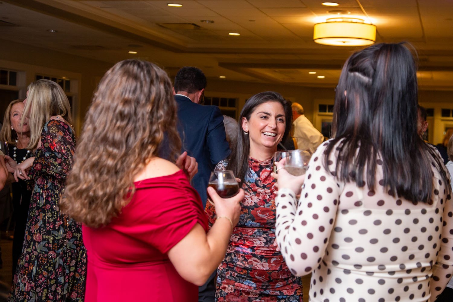 A group of women socializing and enjoying drinks at a party or reception in a well-lit venue.