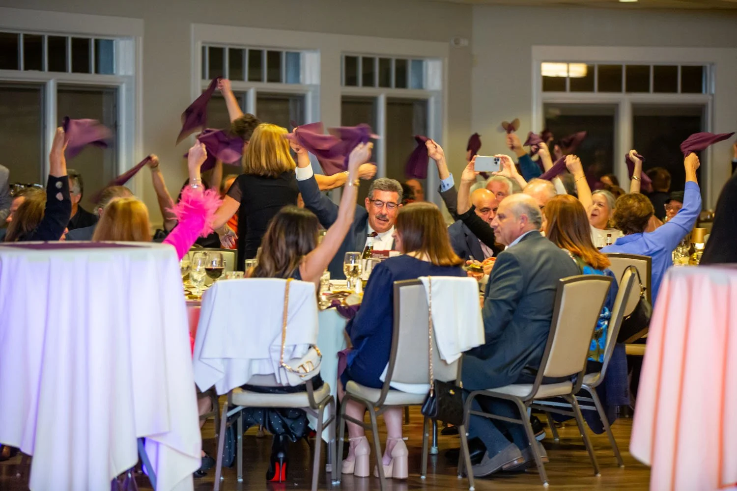 People at a banquet table raising purple napkins in celebration.