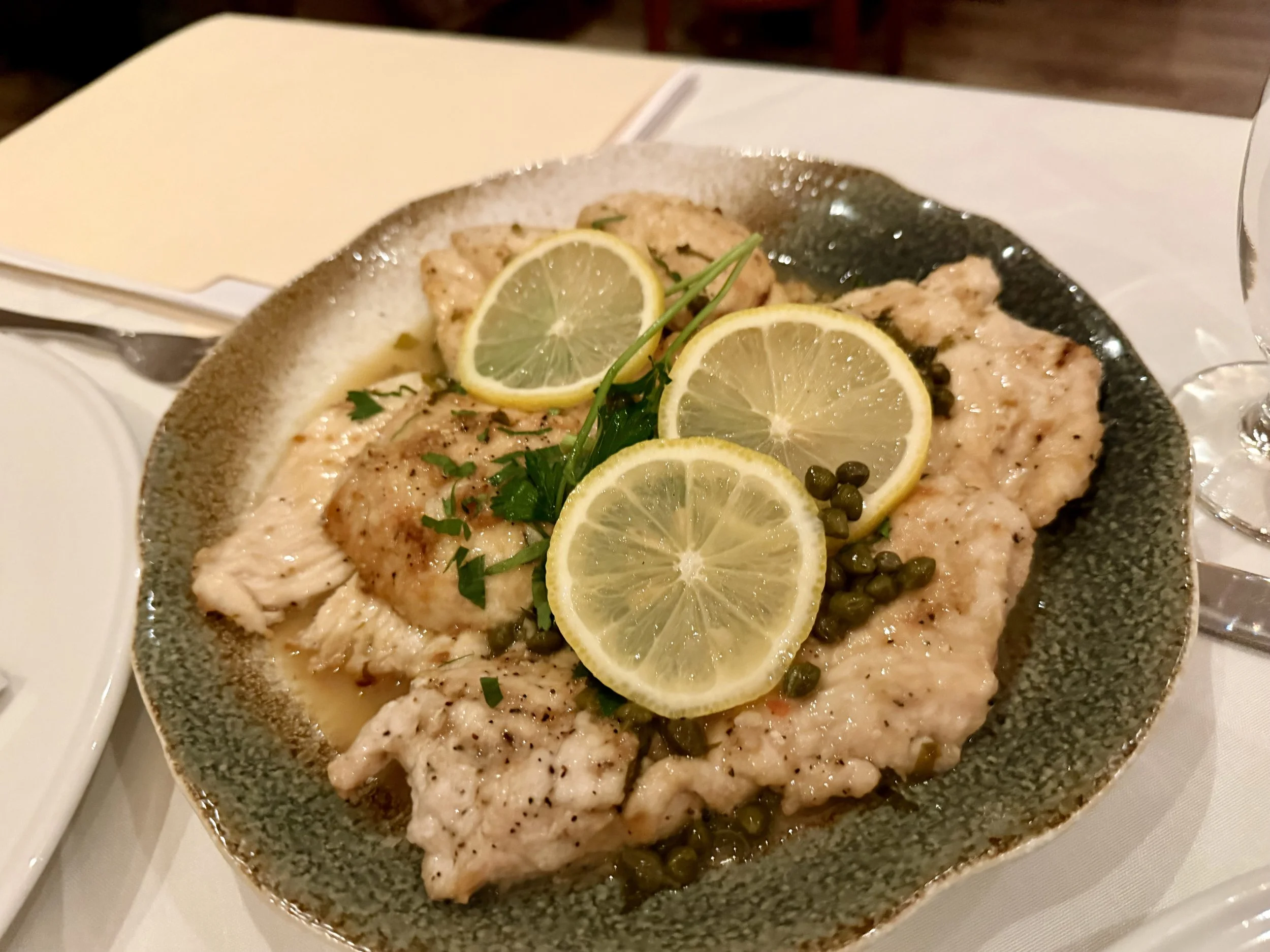 Sliced cooked fish garnished with lemon slices, herbs, and capers on a ceramic plate.