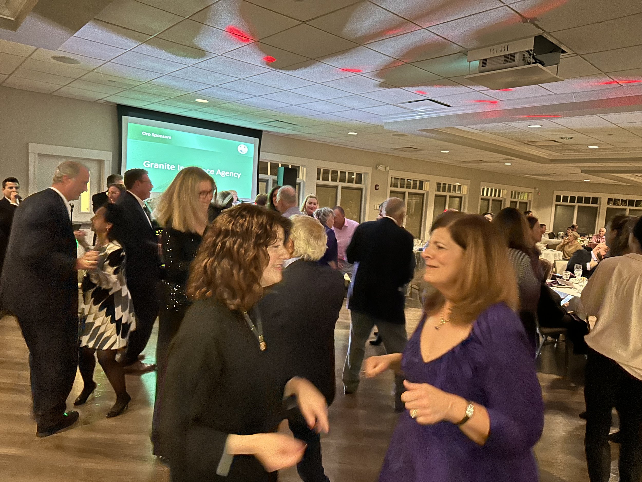 People dancing at an indoor event, with a presentation screen in the background displaying "Granite Insurance Agency."