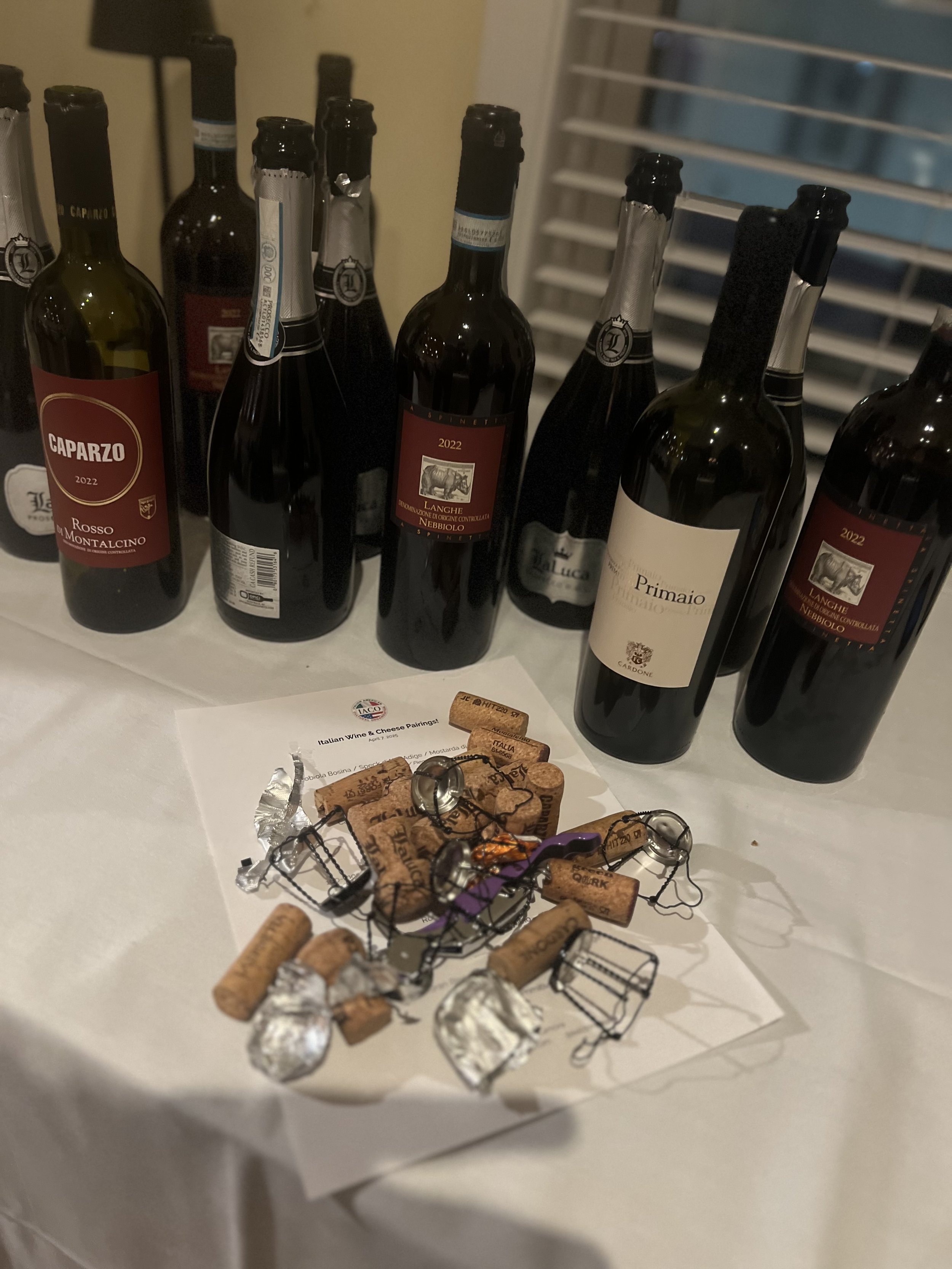 Selection of wine bottles from Italy, including Caparzo Rosso di Montalcino and Langhe Nebbiolo, with wine corks and foil wrappers on a table.