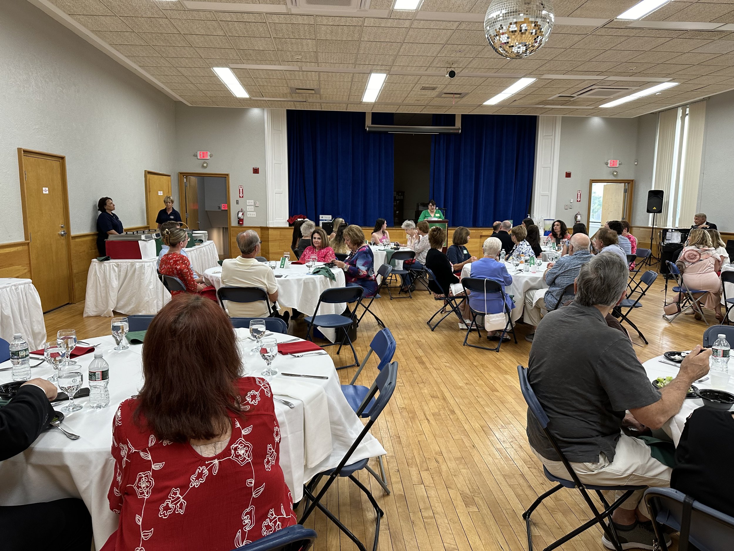 People sitting at round tables in a hall with a blue curtain and disco ball
